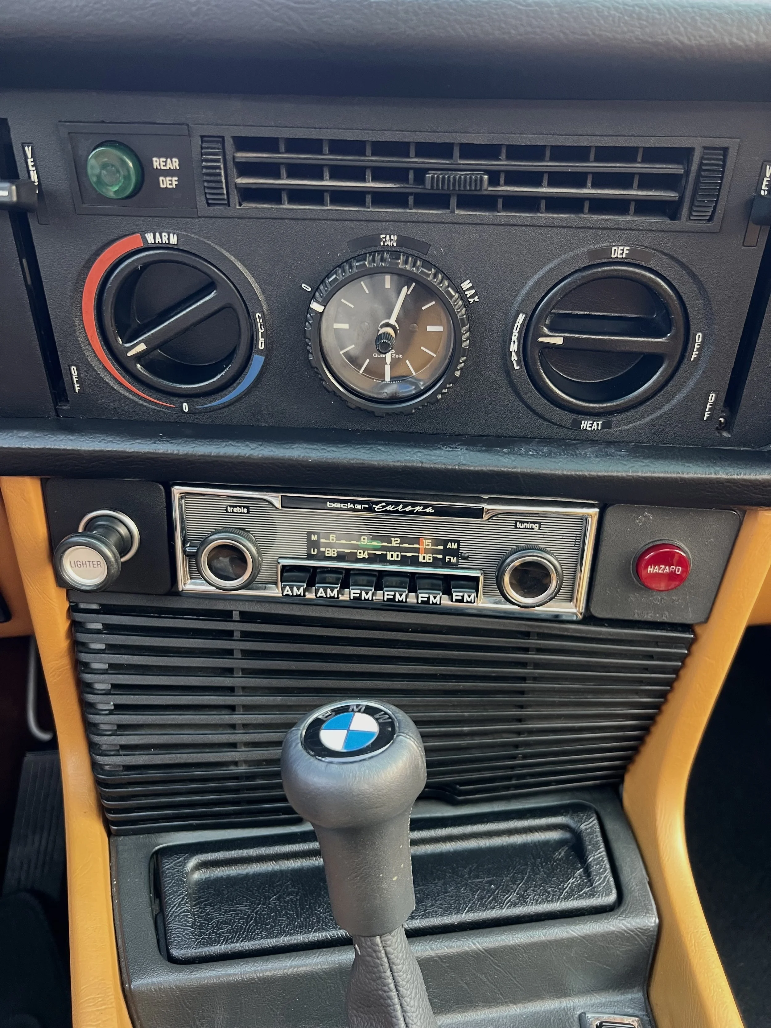 The dashboard of a BMW BMW 630 csi car, showing climate controls, a vintage Becker Europa radio, hazard warning button, and gear shift with BMW logo.