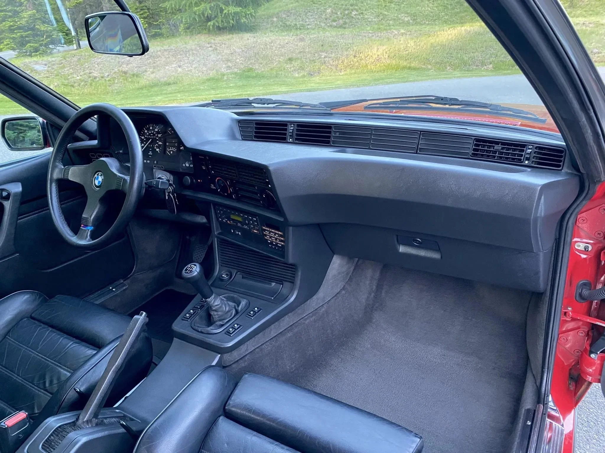Interior of a classic BMW car showing the dashboard, steering wheel, gear shift, and black leather seats.