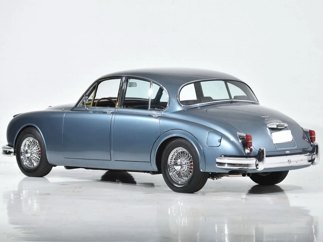 A vintage blue car with wire-spoke wheels, parked against a white background.