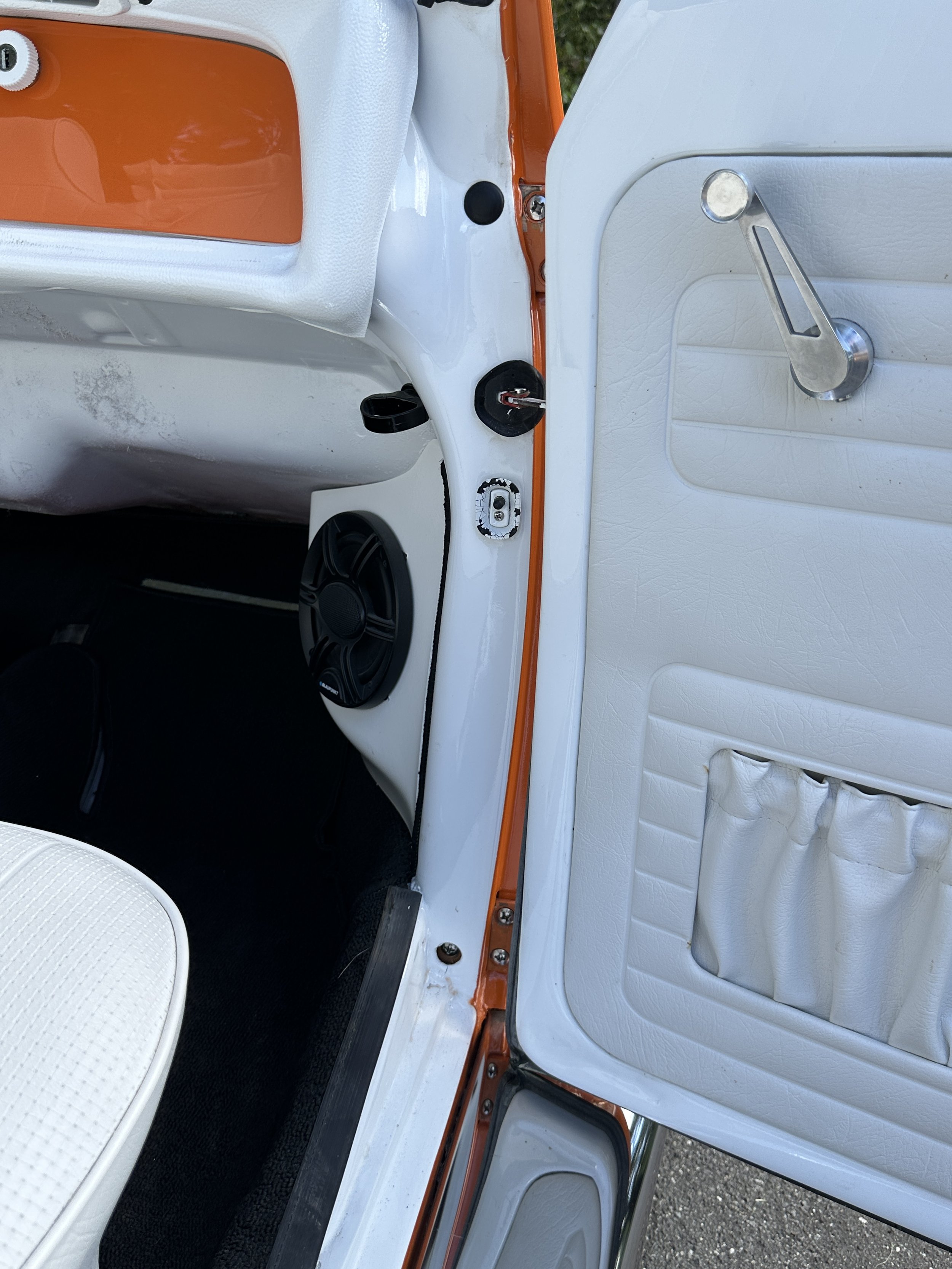 Interior view of a vintage vehicle showing the passenger side door, dashboard, speaker, and part of the seat, with orange and white interior colors.