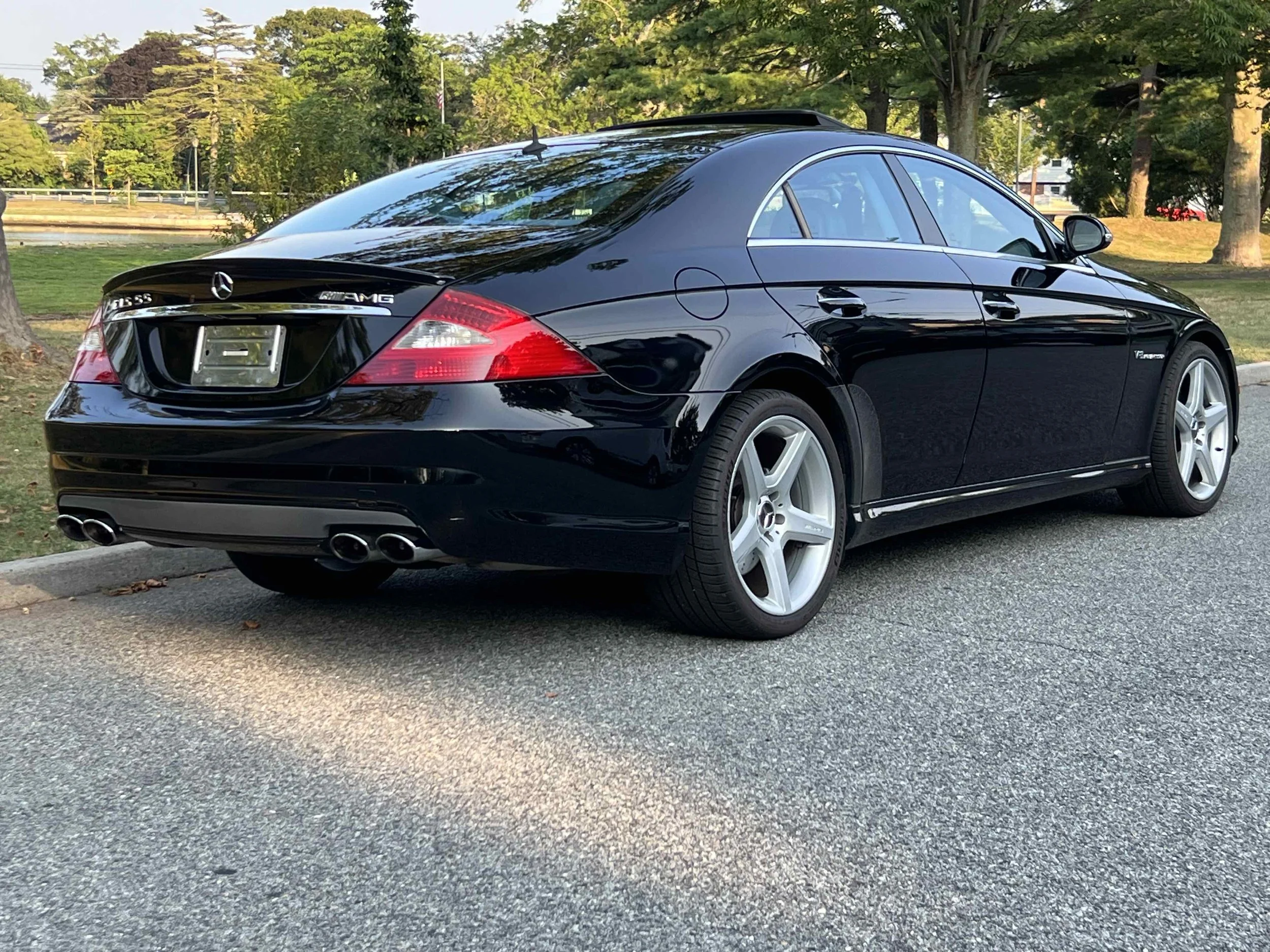 Black Mercedes-Benz CLS55 AMG  parked on a street with trees and a park in the background.