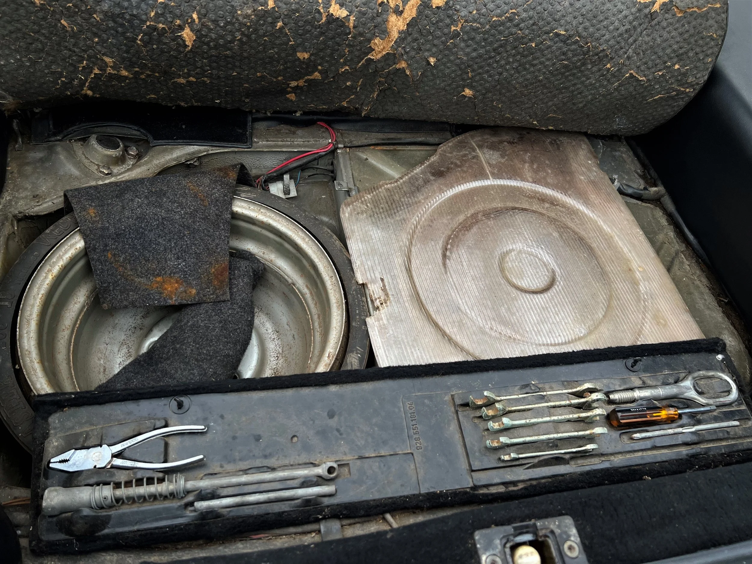 The interior of a car's front seat removed, exposing a damaged speaker, insulation, and various tools including pliers, screwdrivers, and wrenches.