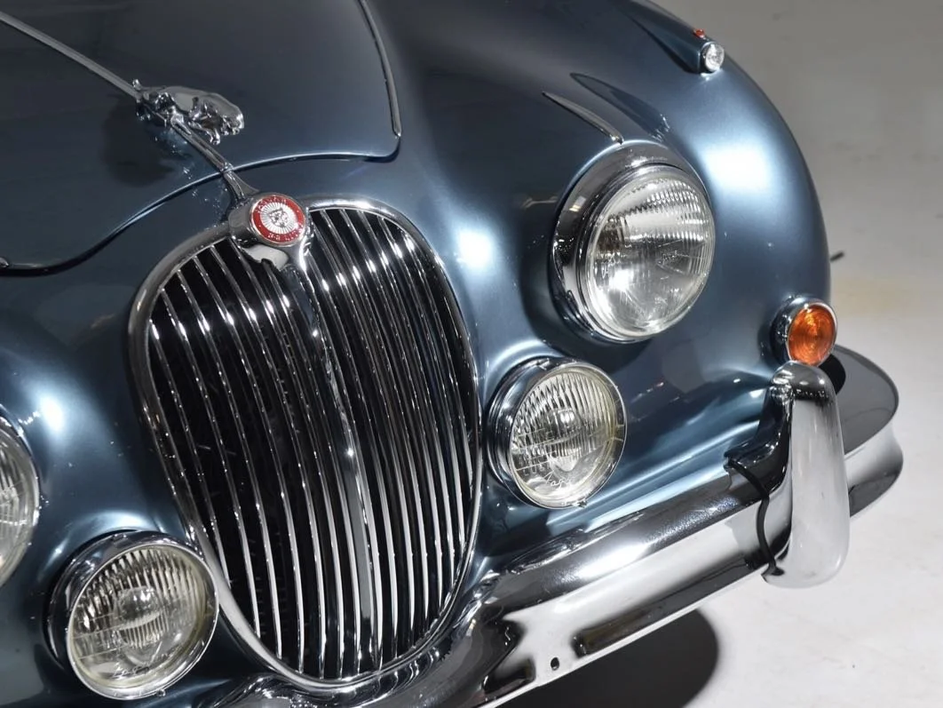 Close-up of the front of a vintage blue car, showing its chrome grille, round headlights, and bumper.