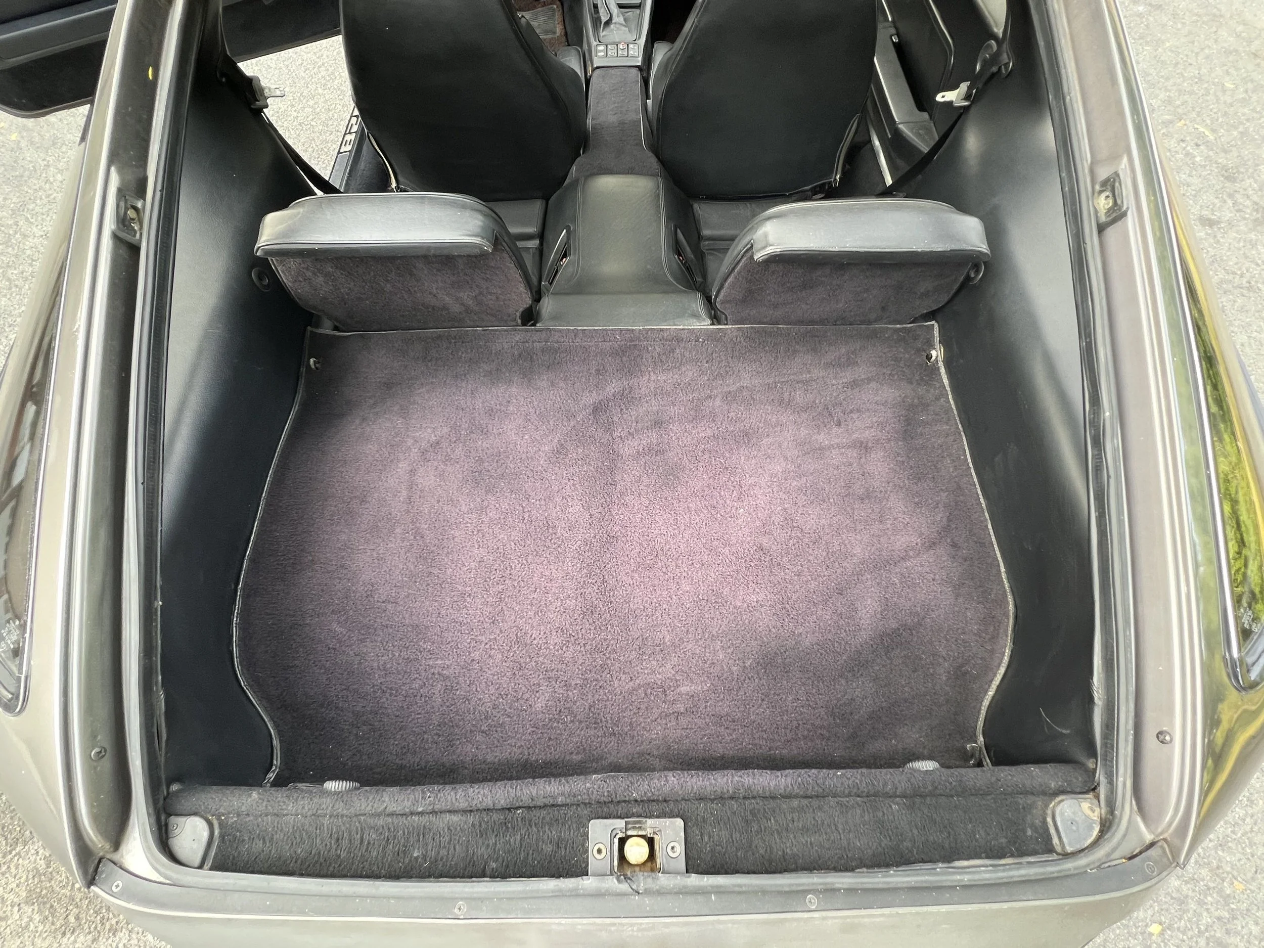 Interior of a vintage DeLorean with the rear seats folded down, showing the cargo area with black carpeting.