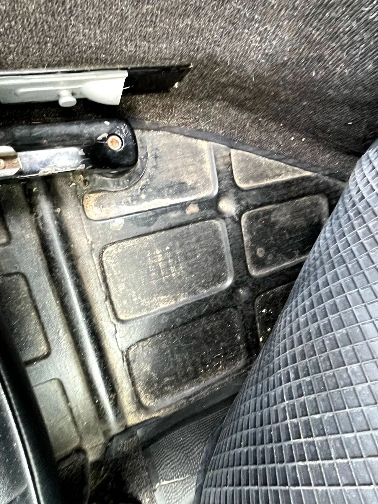 Inside a car showing the dirty floor mat, part of the seat, and the bottom of the dashboard.