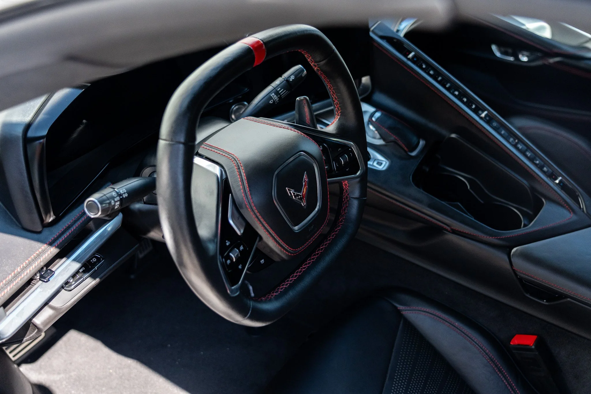Close-up of the steering wheel and dashboard of a Corvette sports car with black leather interior and red stitching.