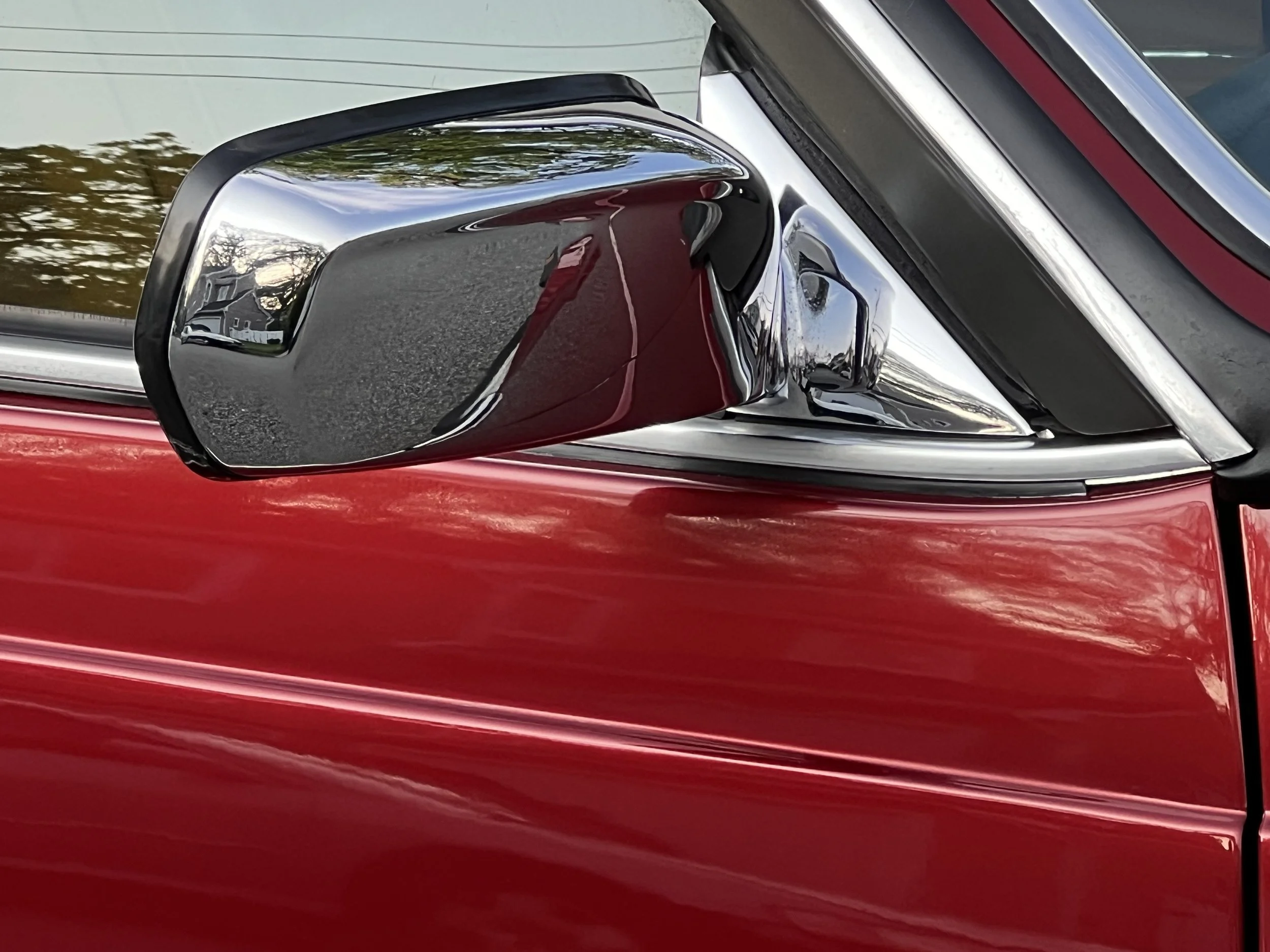 Close-up of a red BMW 630 csi car's side mirror and window with reflections of trees and houses.