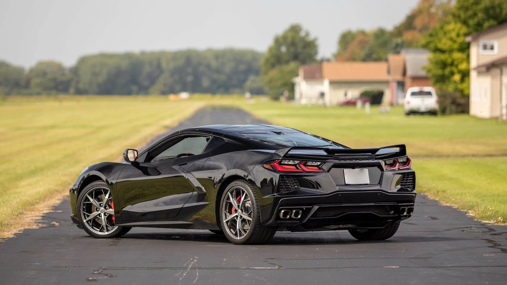 Black sports car parked on a paved road in a suburban area with houses and green trees in the background.
