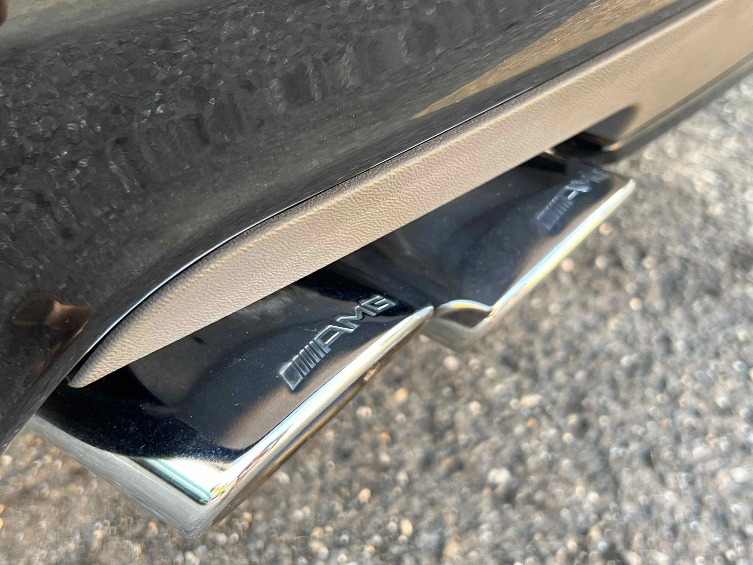 Close-up of a Mercedes-AMG car's rear exhaust pipe with an AMG badge, chrome finish, and dual exhaust tips.