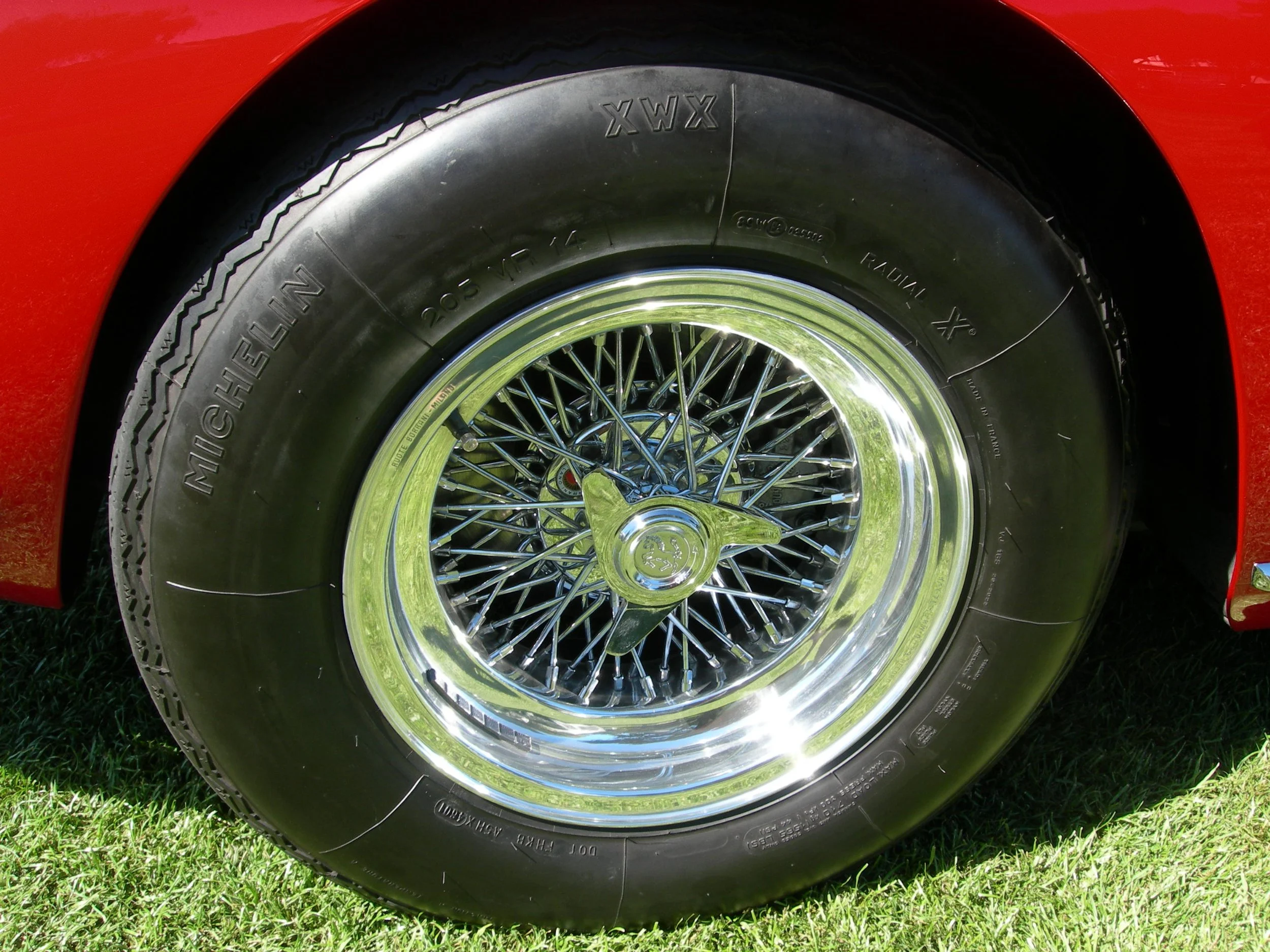 Close-up of a vintage car tire with a shiny wire-spoke wheel and red body in the background.