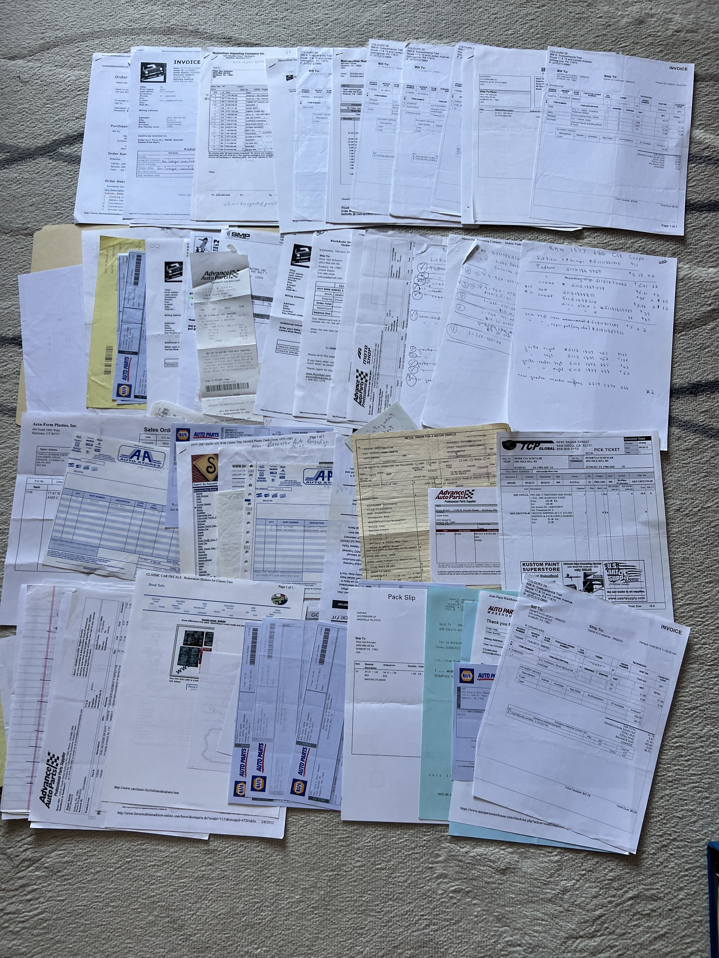 A large collection of scattered invoices, receipts, and documents, laid out on a beige carpet belonging to a 1977 BMW 630 csi.
