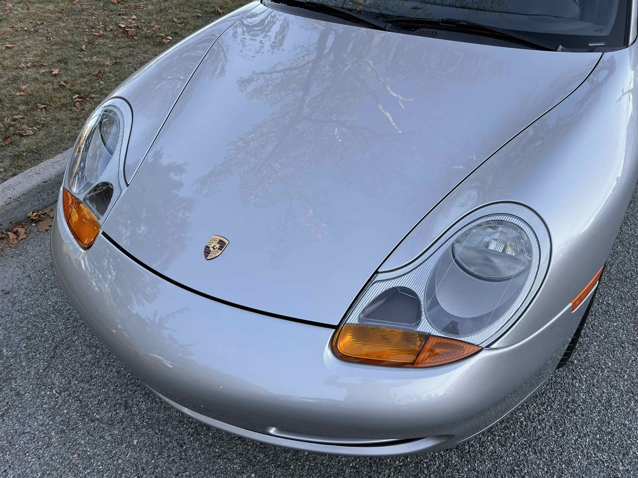 Silver Porsche sports car viewed from front with the hood, headlights, and Porsche emblem visible on the hood.