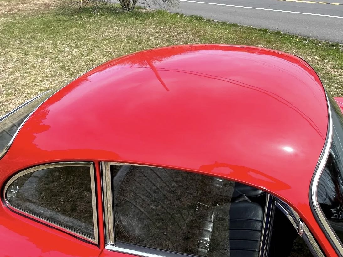 Close-up of the red painted roof of a vintage car parked on grass near a road