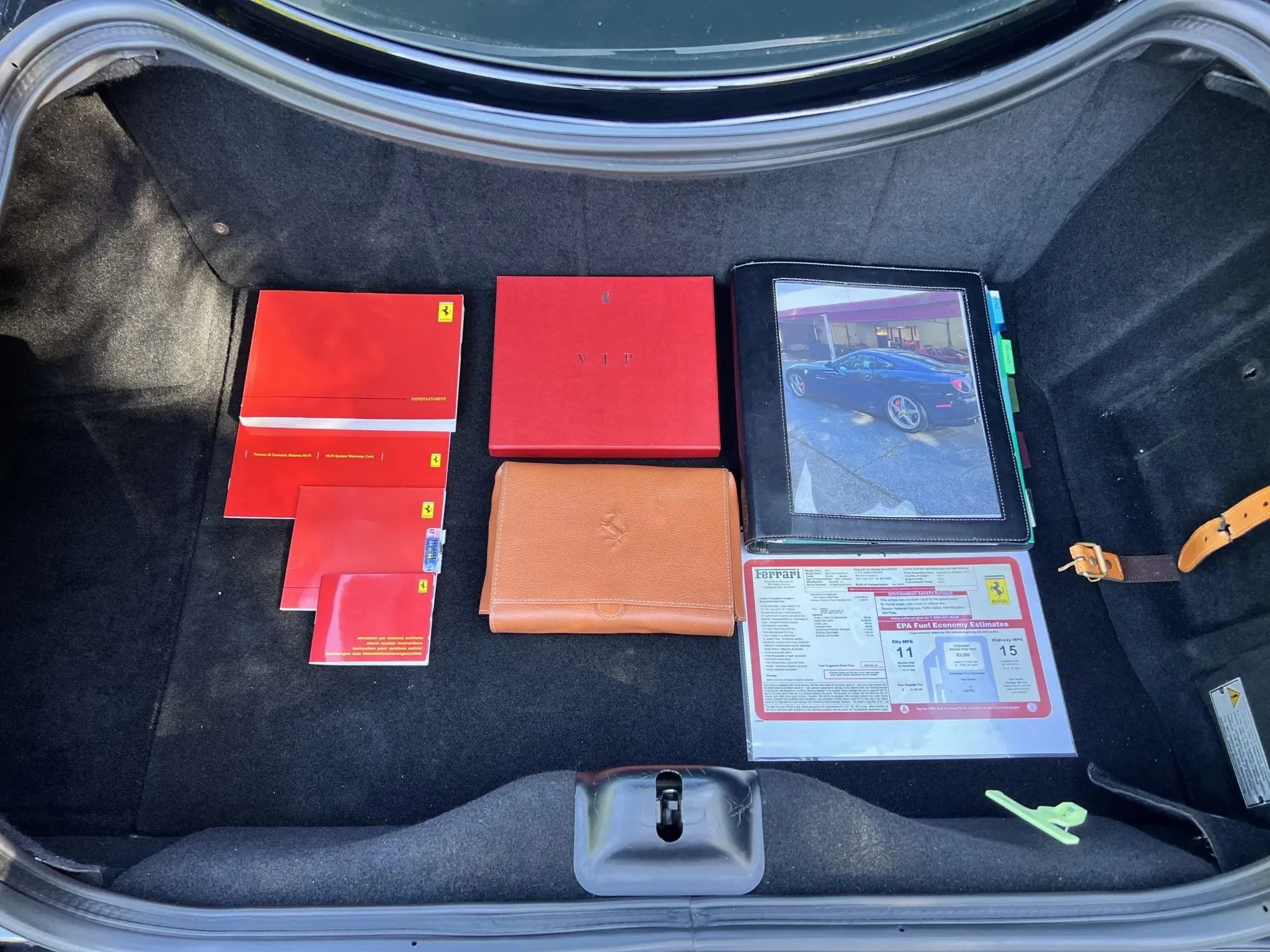 Car trunk with various Ferrari documents, brochures, and magazines, including a Carfax report and a folder with a photo of a black Ferrari on the cover.