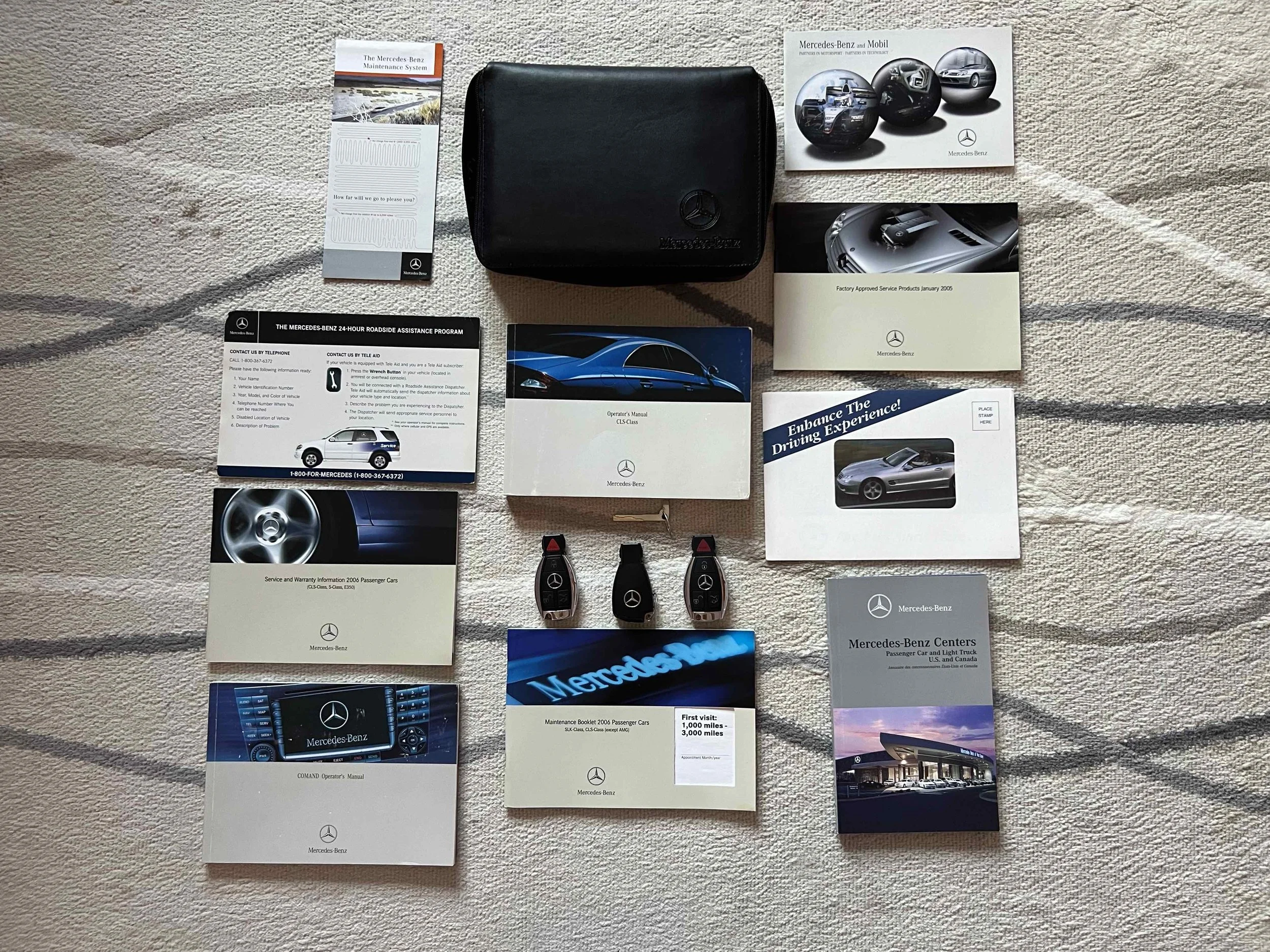 Collection of Mercedes-Benz car manuals, booklets, key fobs, and accessories arranged on a beige textured surface.