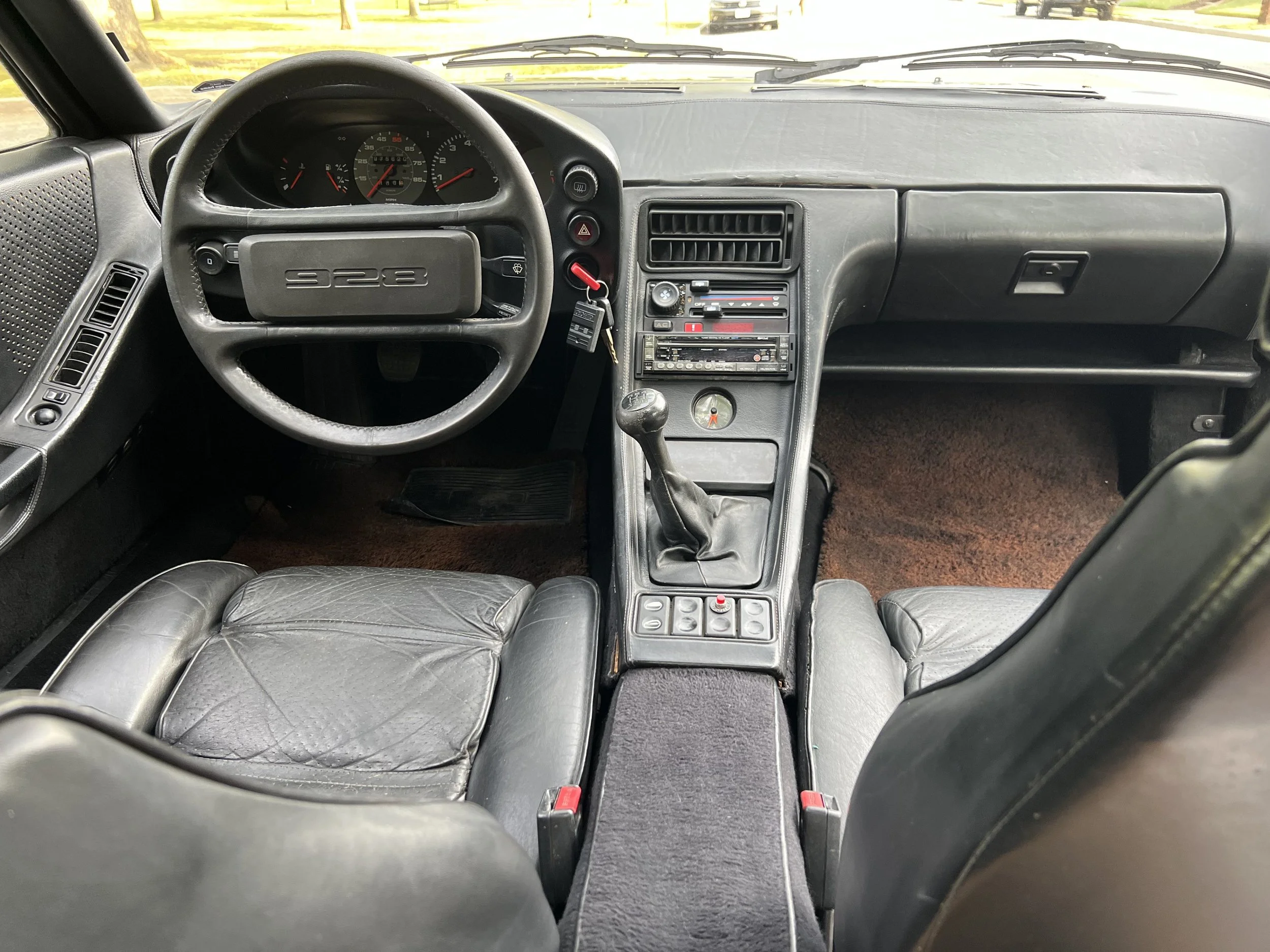 Interior of a vintage sports car with black leather seats, analog dashboard, manual gear shift, and various control buttons.