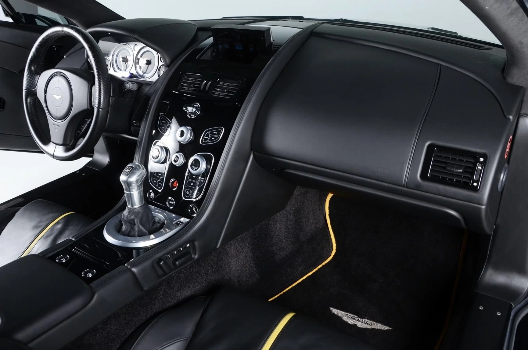 The interior of a luxury sports car, featuring a black dashboard, a leather-wrapped steering wheel, a gear shift, and a digital display screen. The dashboard includes various control buttons and a central console.