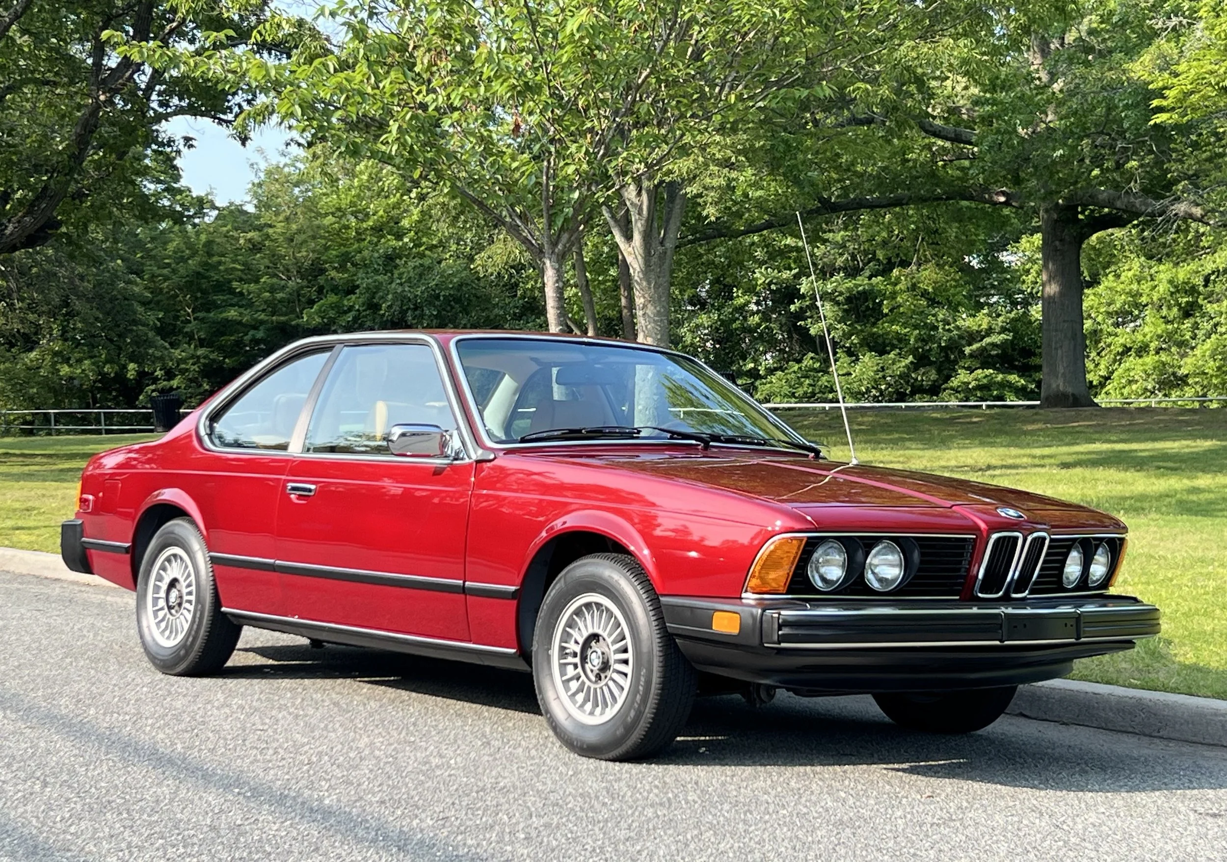 Ruby Red 1977 BMW 630 csi on display in park with trees and grass in background for sale at FlowHaus