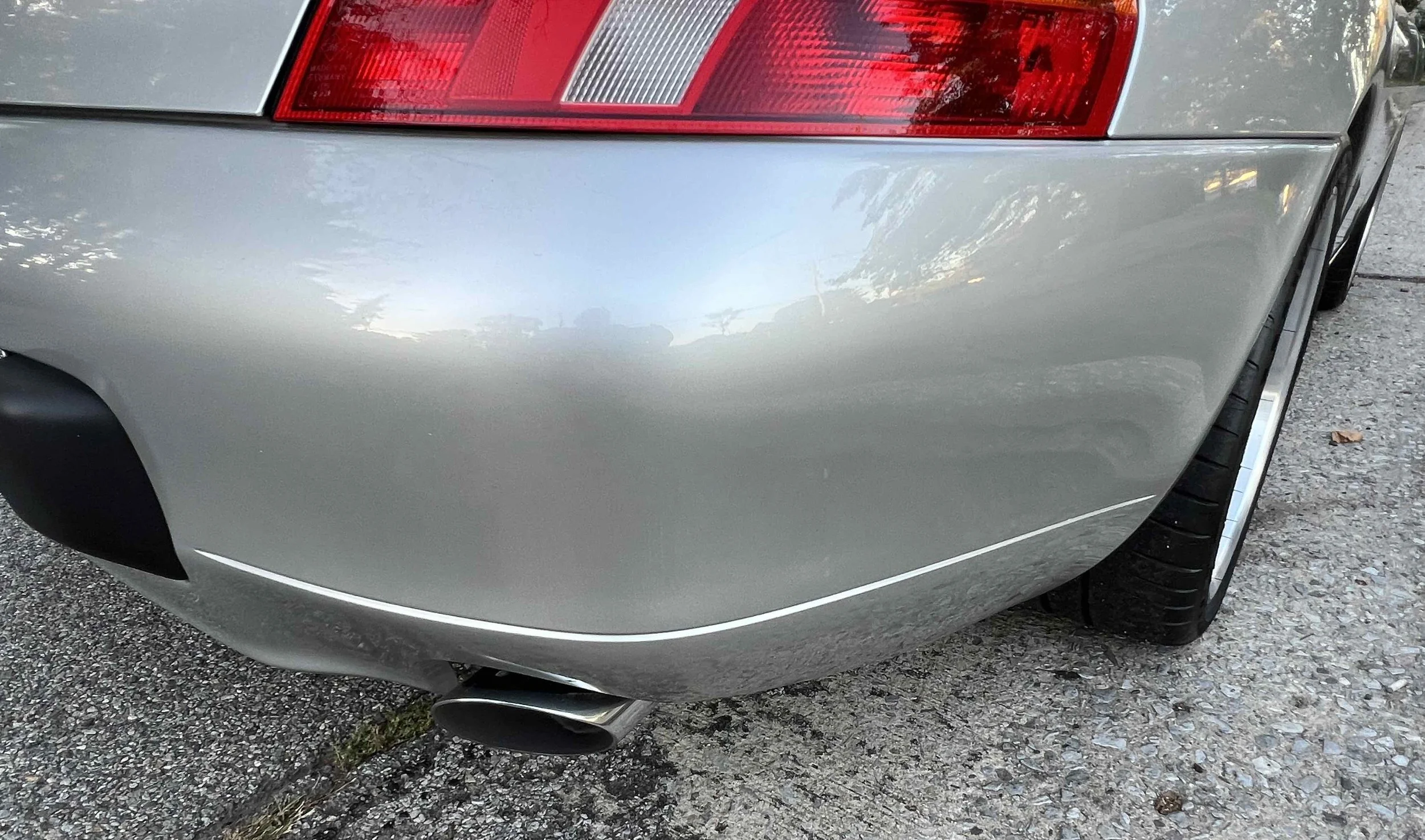 Rear right side of a silver car showing tail light, bumper, exhaust pipe, and part of the tire.