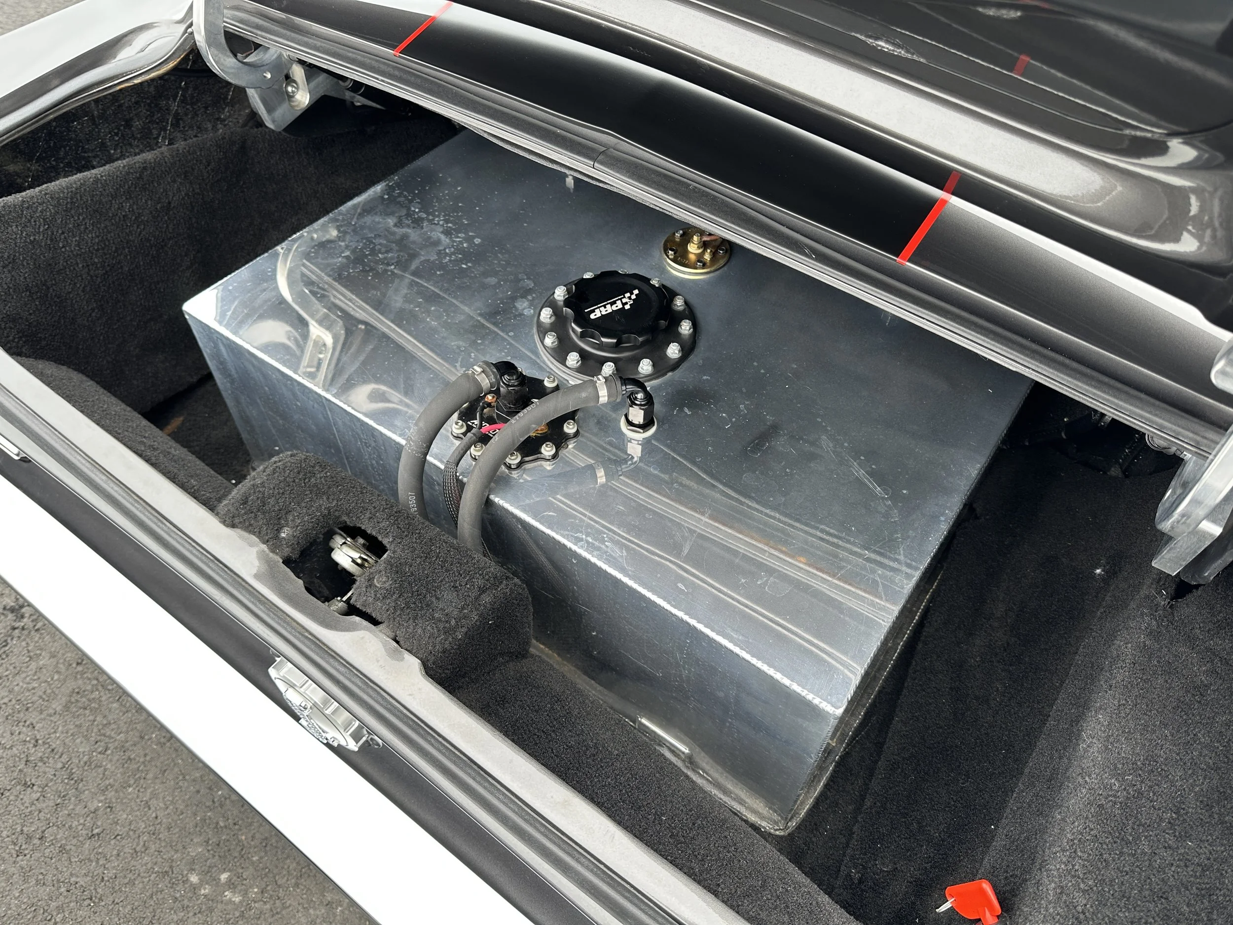 A fuel cell with hoses and a cap inside a vehicle trunk, likely part of a race car.