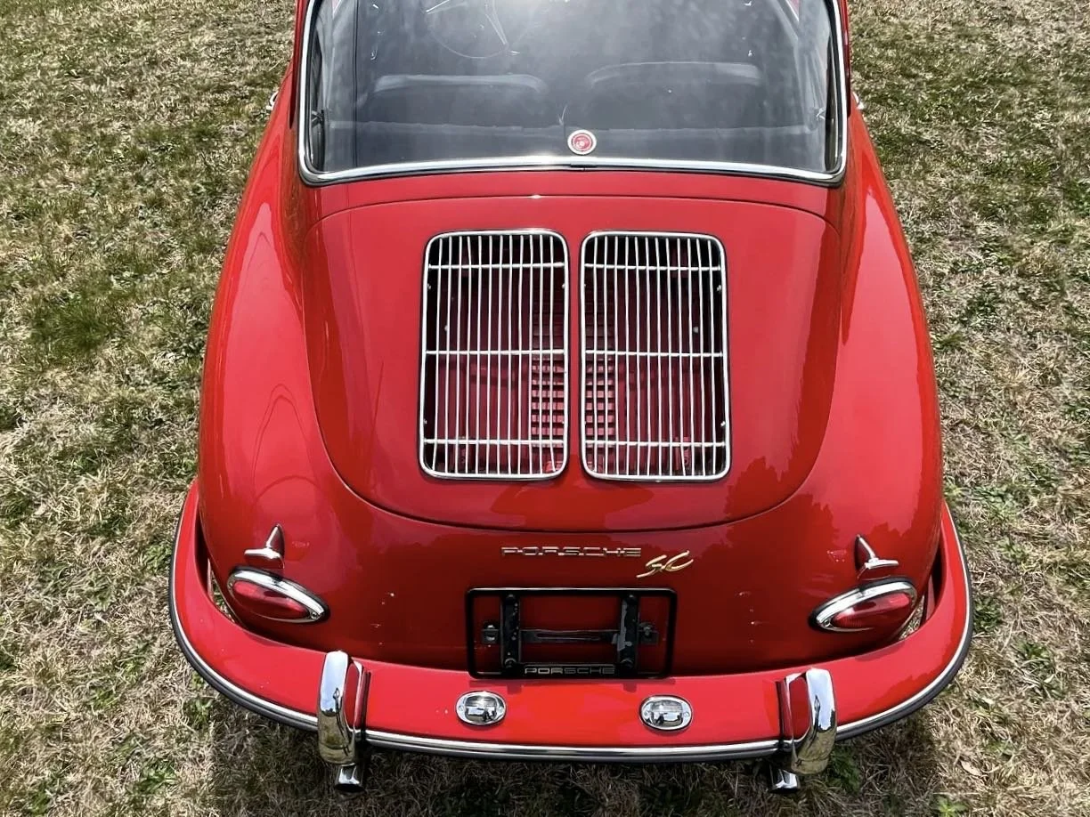 Top view of a red vintage Porsche 356 with a rear engine grille and chrome detailing, parked on grass.