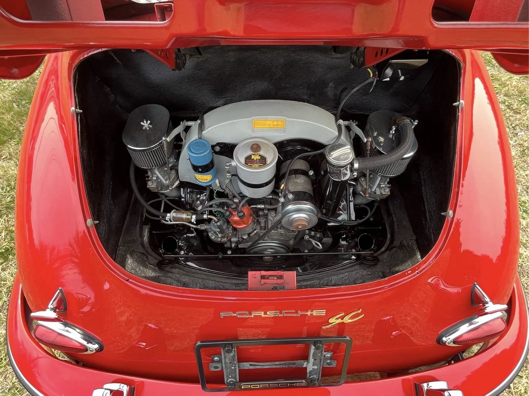 View of the front trunk of a red Porsche 911 with the engine exposed, showing various engine components including filters, belts, and hoses.