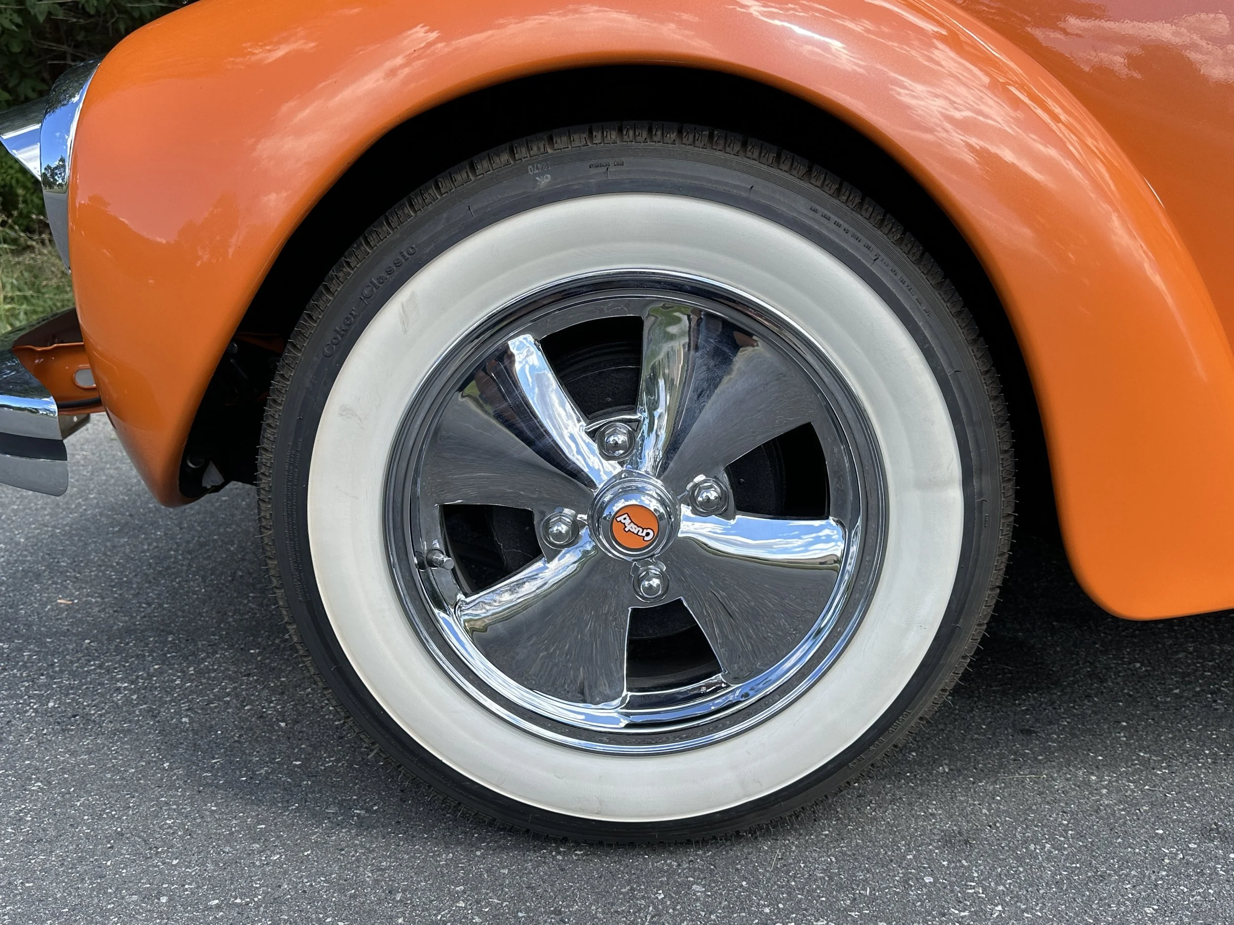 Close-up of a classic orange car wheel with a whitewall tire and shiny chrome hubcap.