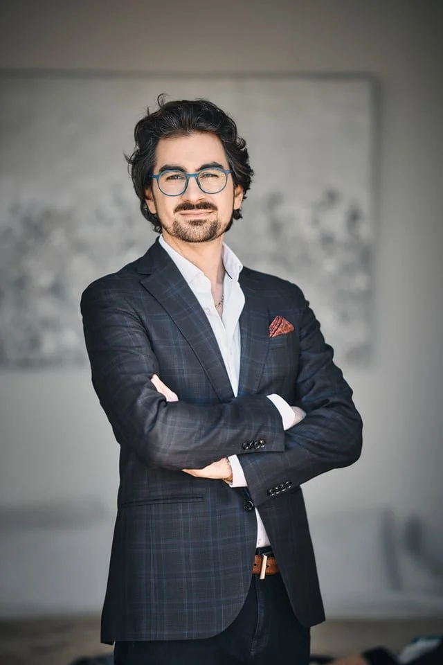 Brian Miller founder and principal consultant of Clarity Up, wearing a dark plaid blazer, white shirt, and a pocket square, standing with arms crossed in a modern office or conference room.