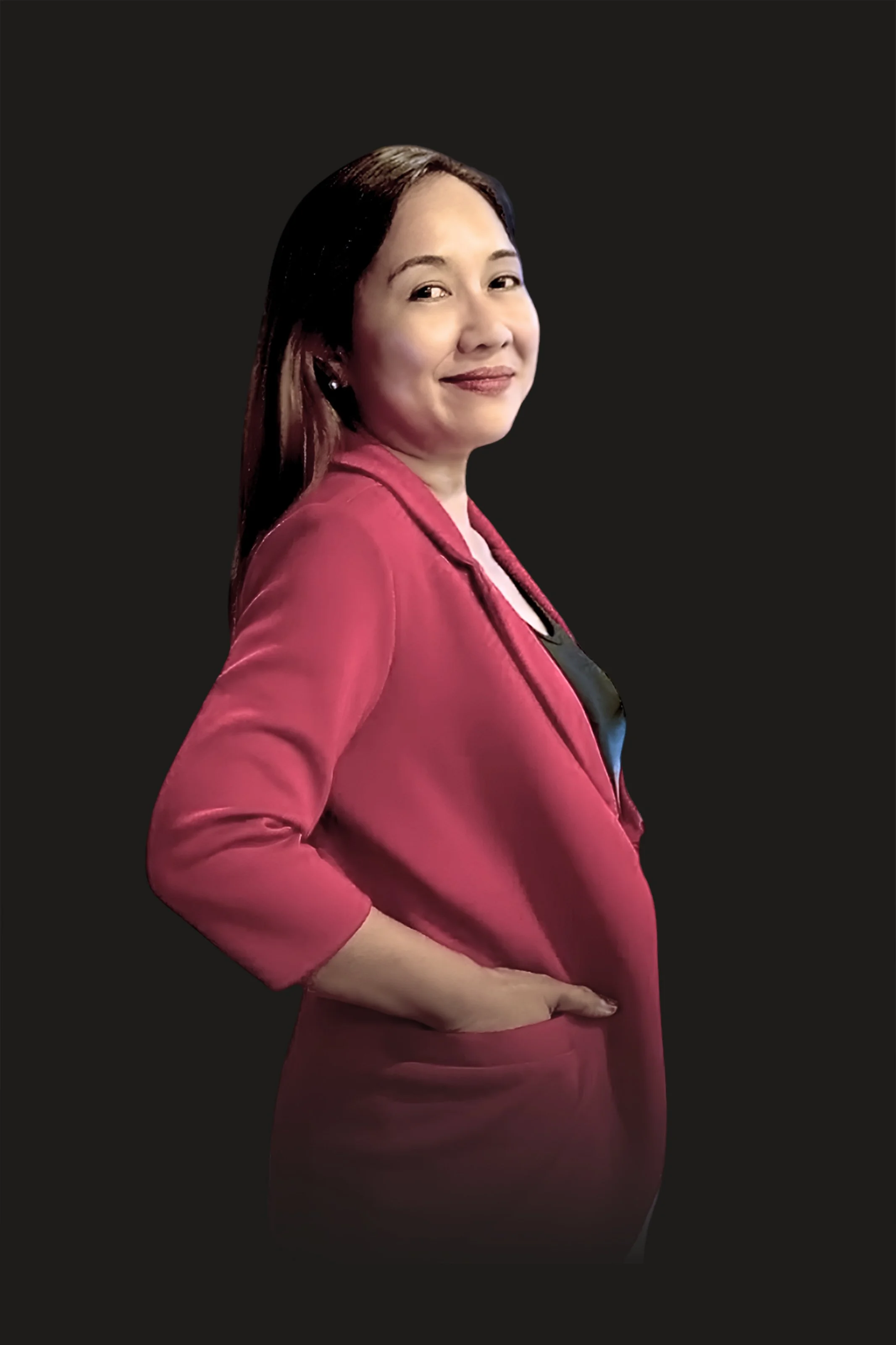 A woman with long dark hair wearing a red blazer and matching skirt, standing against a plain black background, smiling slightly with her hand resting on her hip.