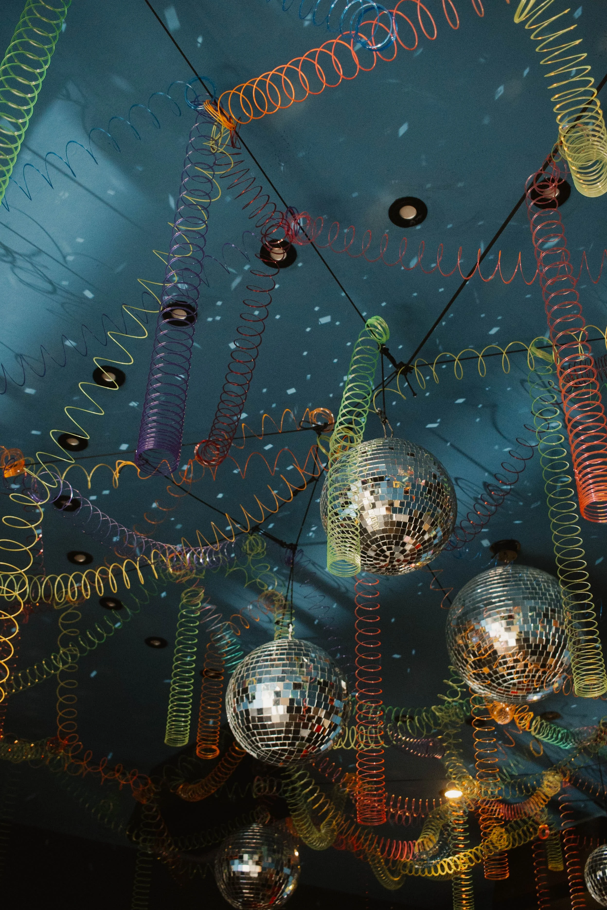 Colorful coiled decorations and disco balls hanging from a blue ceiling.