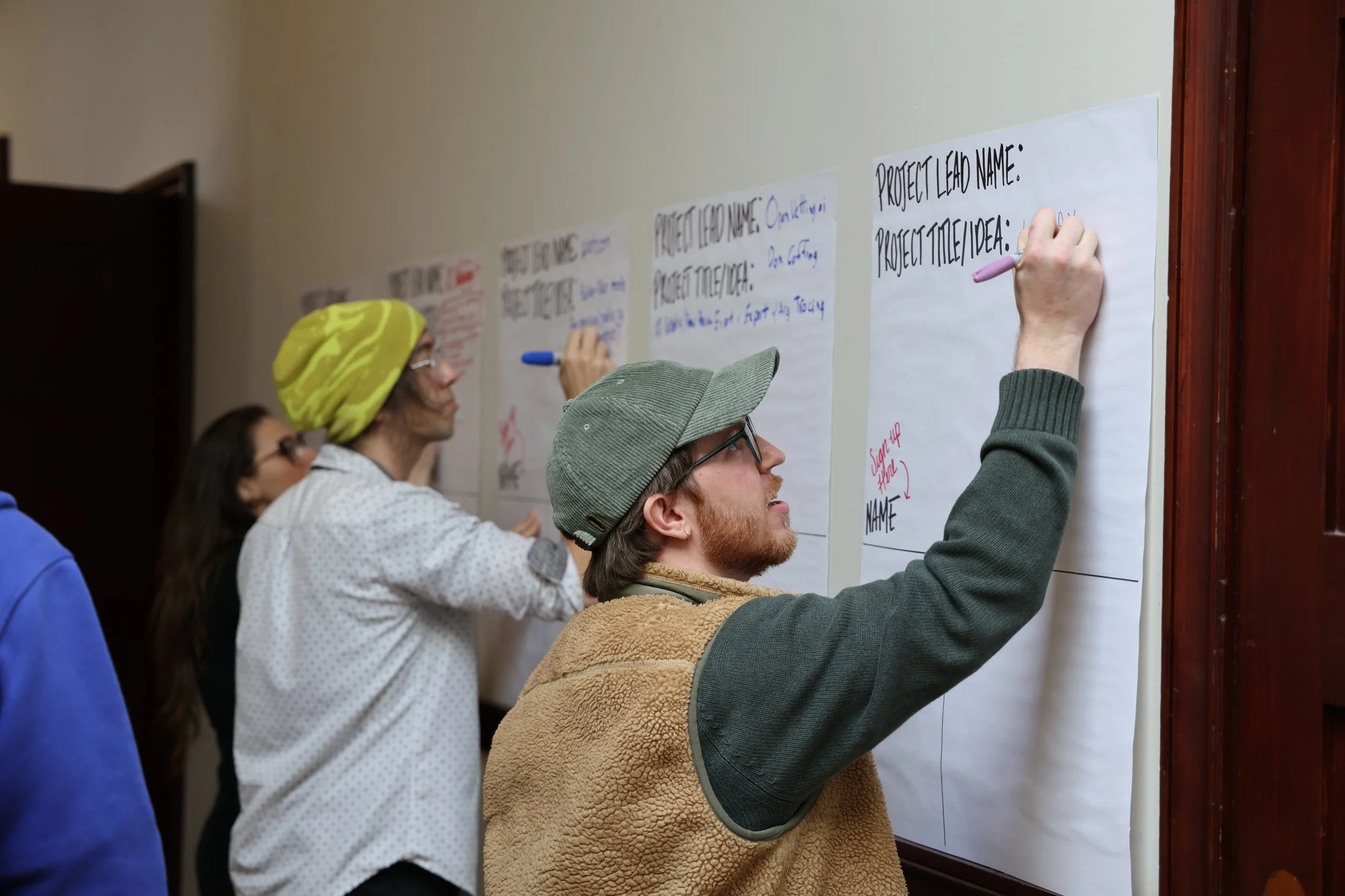 Group of people writing on large sheets of paper posted on a wall, participating in a workshop or brainstorming session.