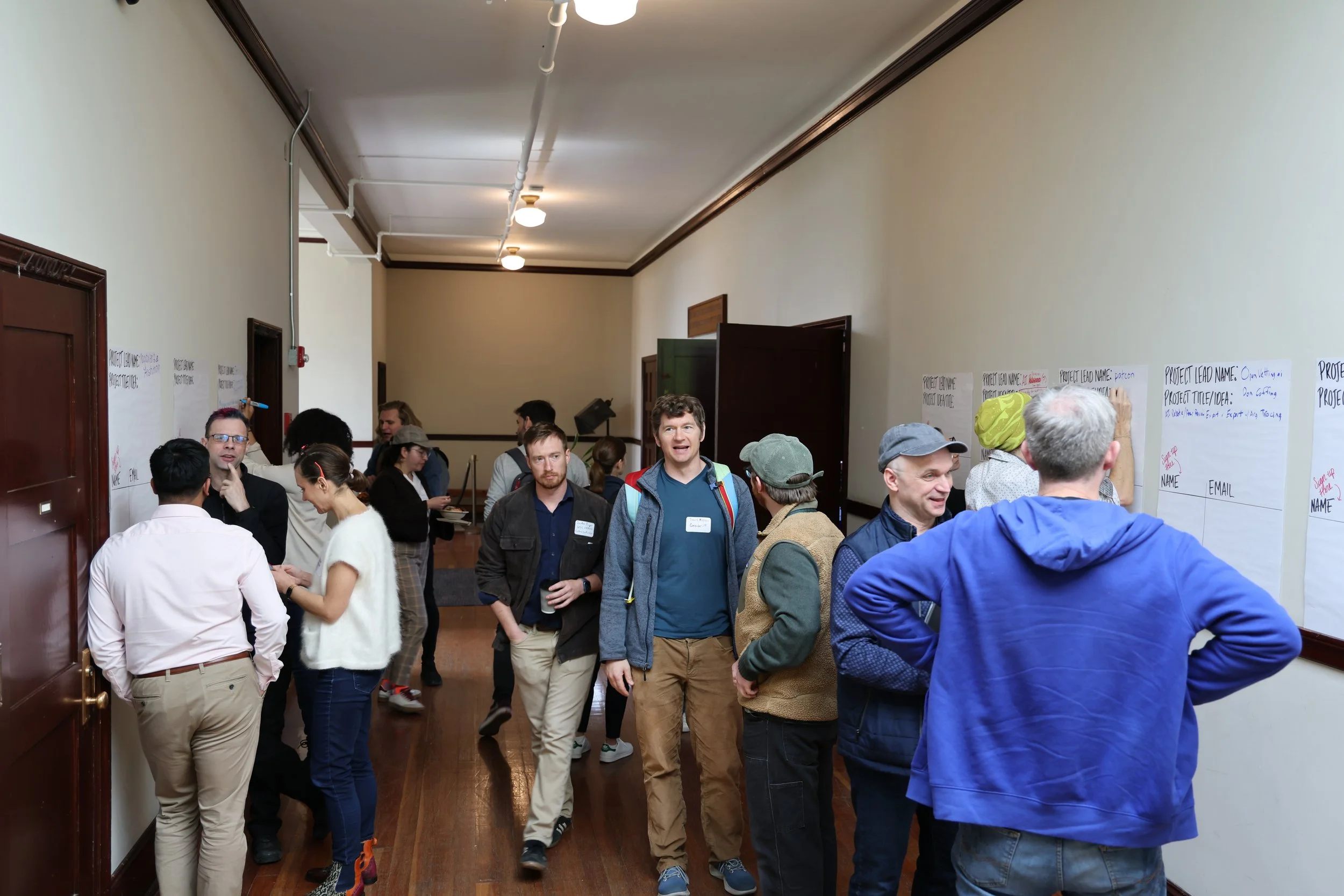 People participating in a workshop or seminar, writing and engaging in discussion in a corridor with posters on the wall.