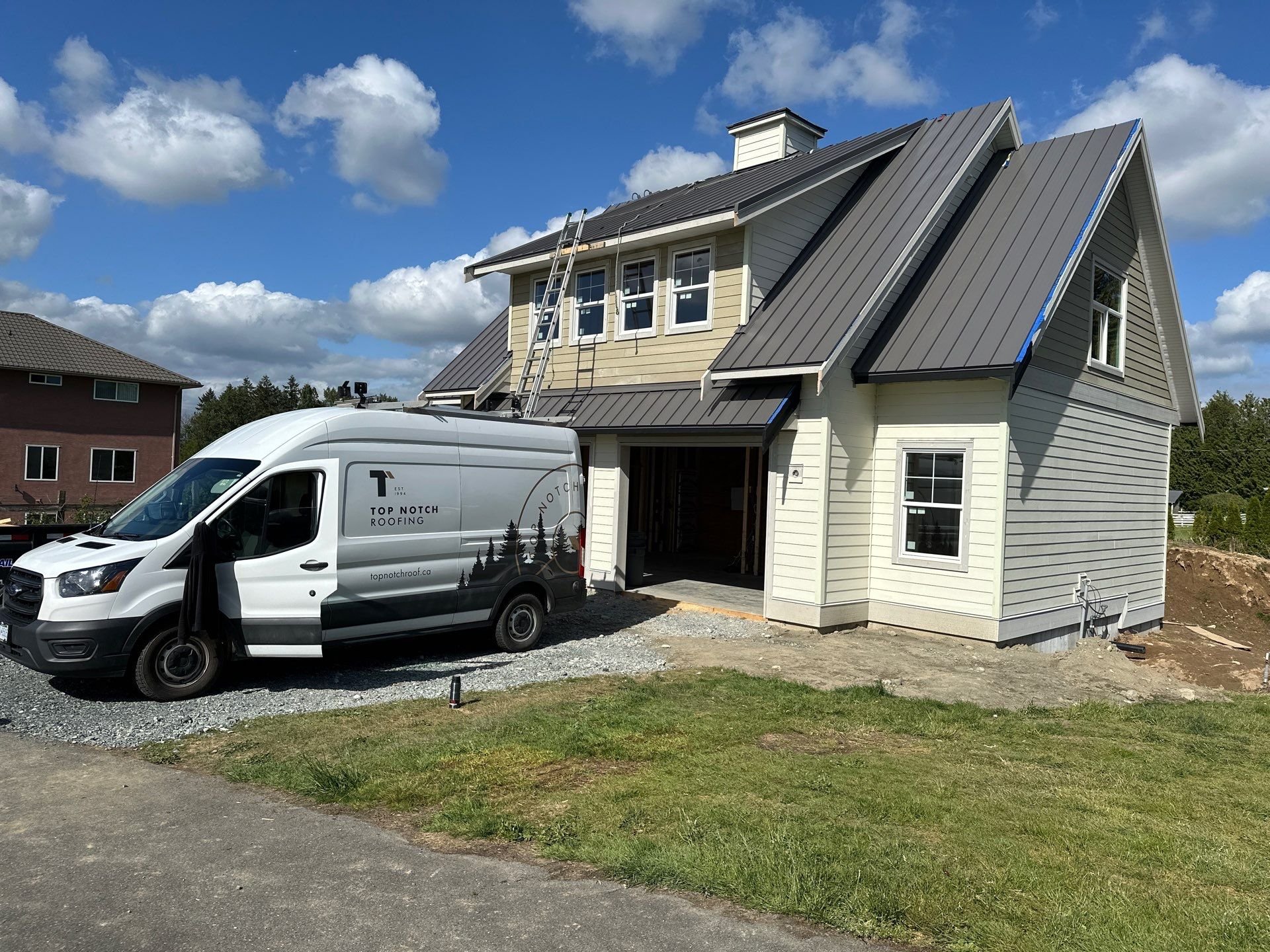 A Top Notch Roofing Car is standing in front of a residential home in Aldergrove, BC. Ready to install a new metal roof.