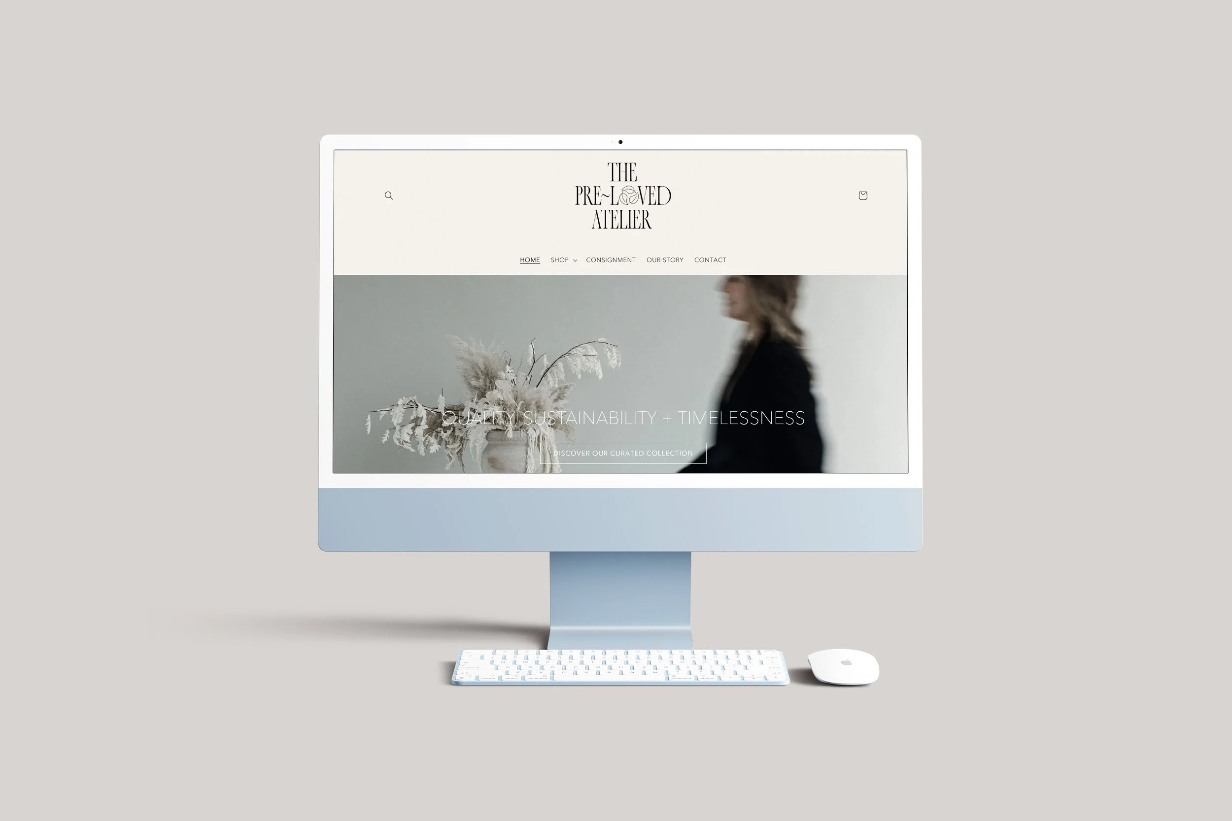 An Apple iMac computer displaying a website for The Pre-Loved Atelier, a minimalist fashion boutique, with a white keyboard and magic mouse against a light gray background.