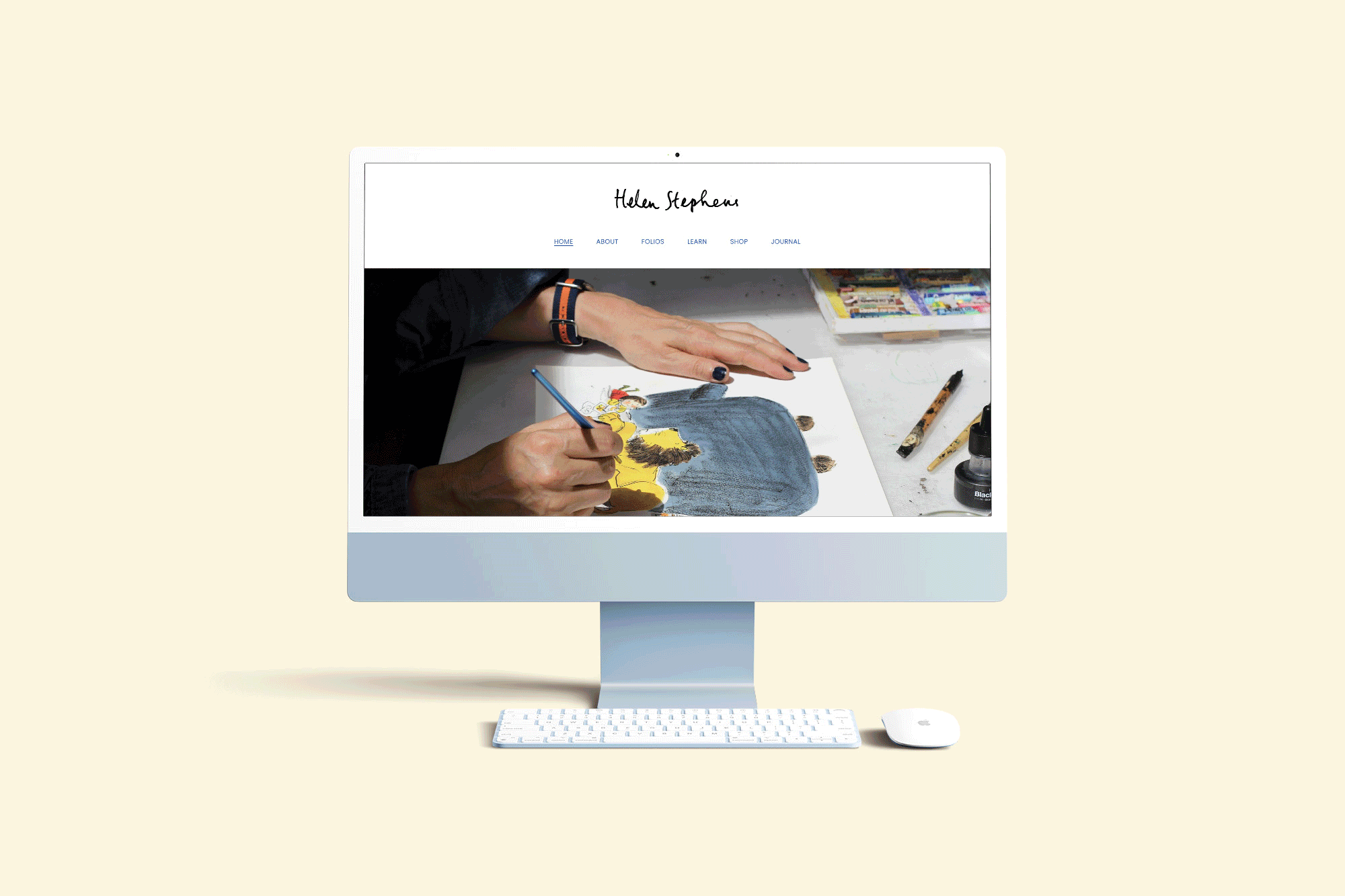 Computer monitor displaying a website with an artist painting a colorful illustration on paper, surrounded by art supplies on a desk.