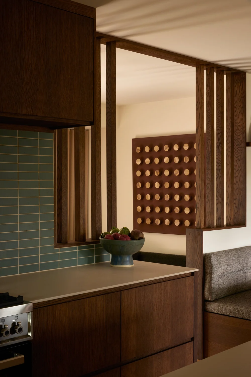 Kitchen with wooden cabinets, a bowl of fresh fruit, a blue tiled backsplash, and decorative wood paneling.