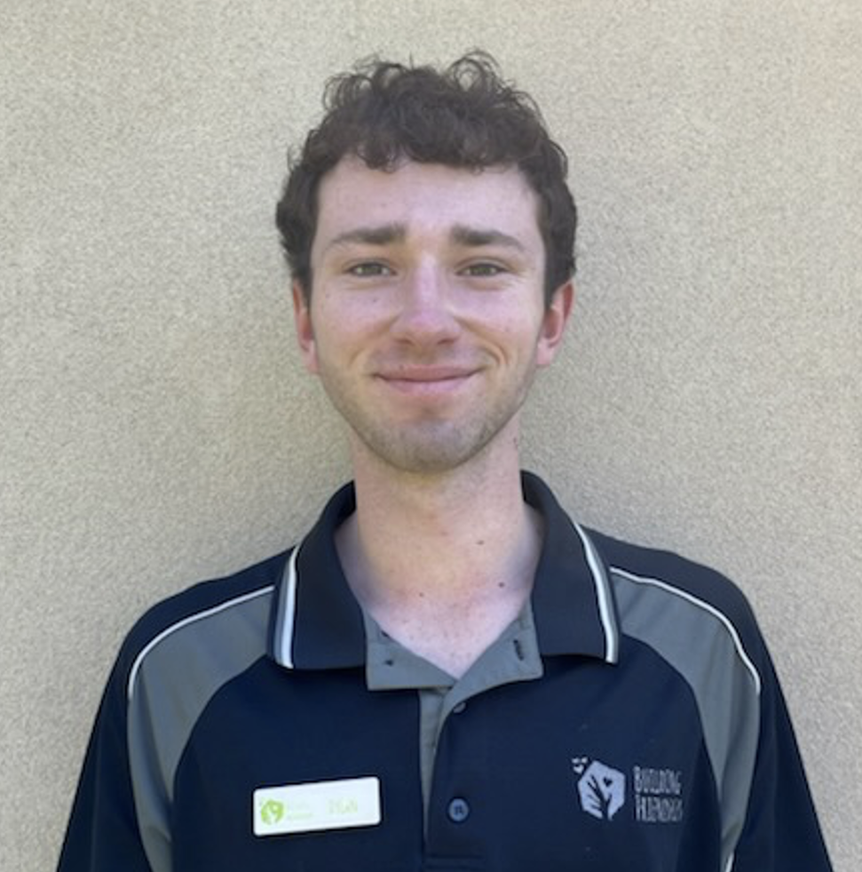 A woman with blonde hair wearing a dark blue polo shirt with gray accents and the logo and text 'Building Friendships,' standing outdoors against a beige wall.