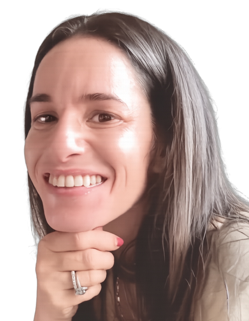 A Jewish Woman with dark hair, smiling, with her chin resting on her hand, wearing a beige jacket and a ring on her finger, indoors near a wooden partition and window.