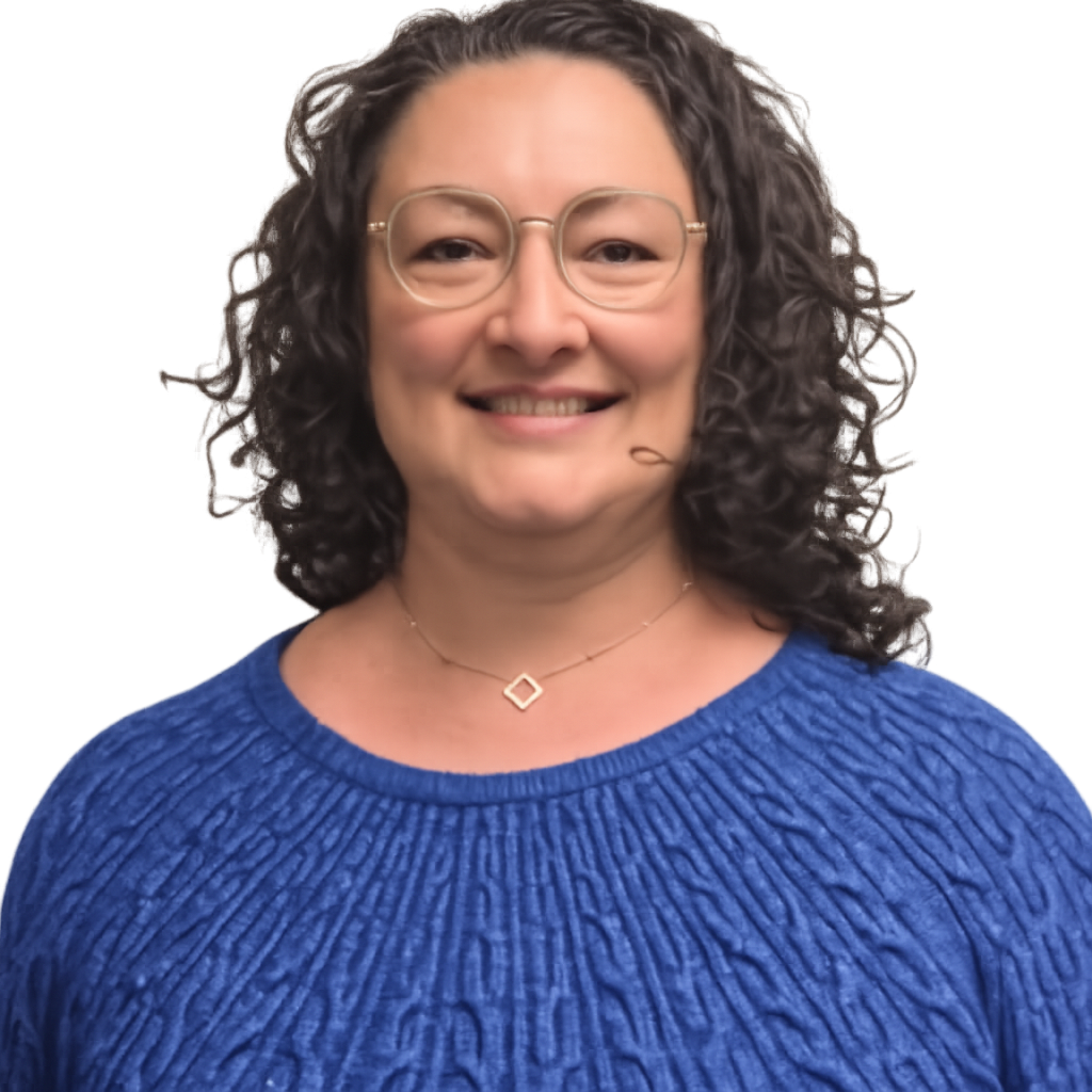 A woman with curly dark hair wearing glasses and a blue knitted sweater smiling in front of a beige textured wall.