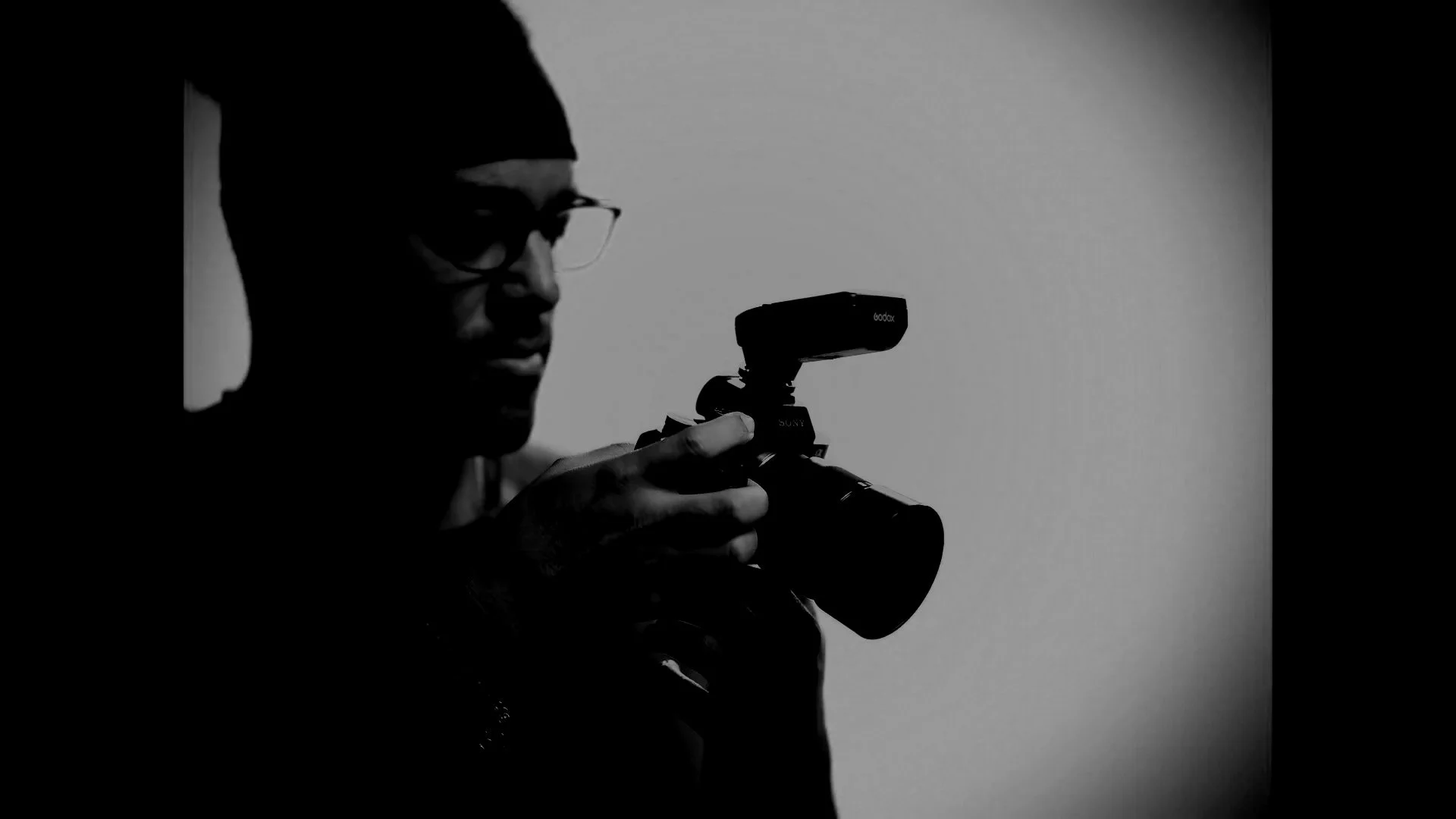 Black and white silhouette of a person wearing glasses and a beanie, holding a camera with a mounted microphone. Content strategy, creative strategy, online visibility, Glowing Moon Media.