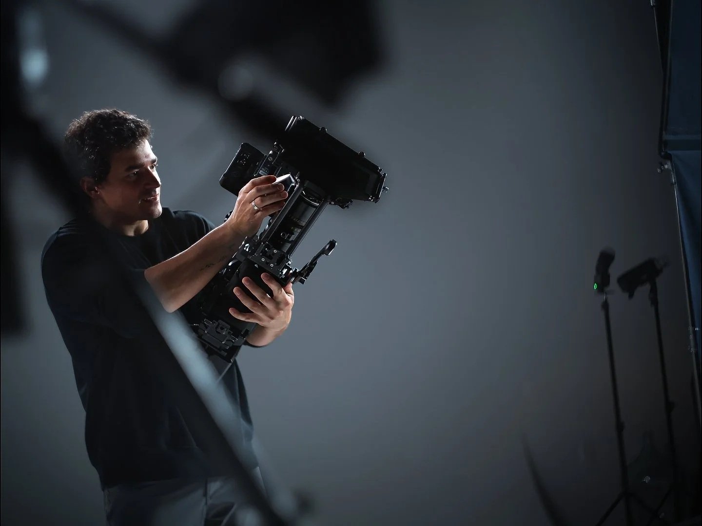 A person holding a professional camera in a studio setting, standing near lighting equipment.
