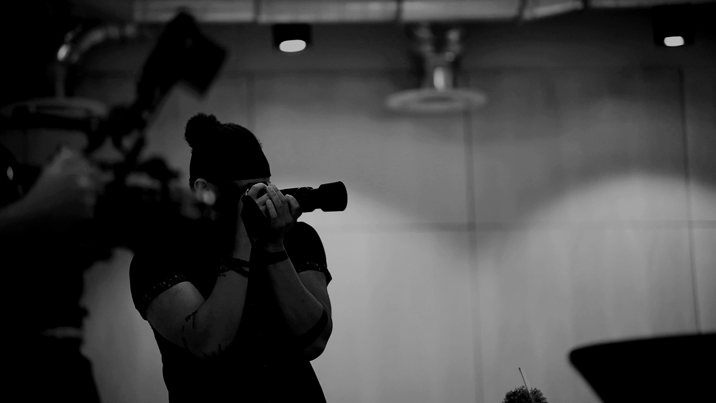 A person holding a camera and taking a photo in a room with overhead lighting, seen in silhouette.