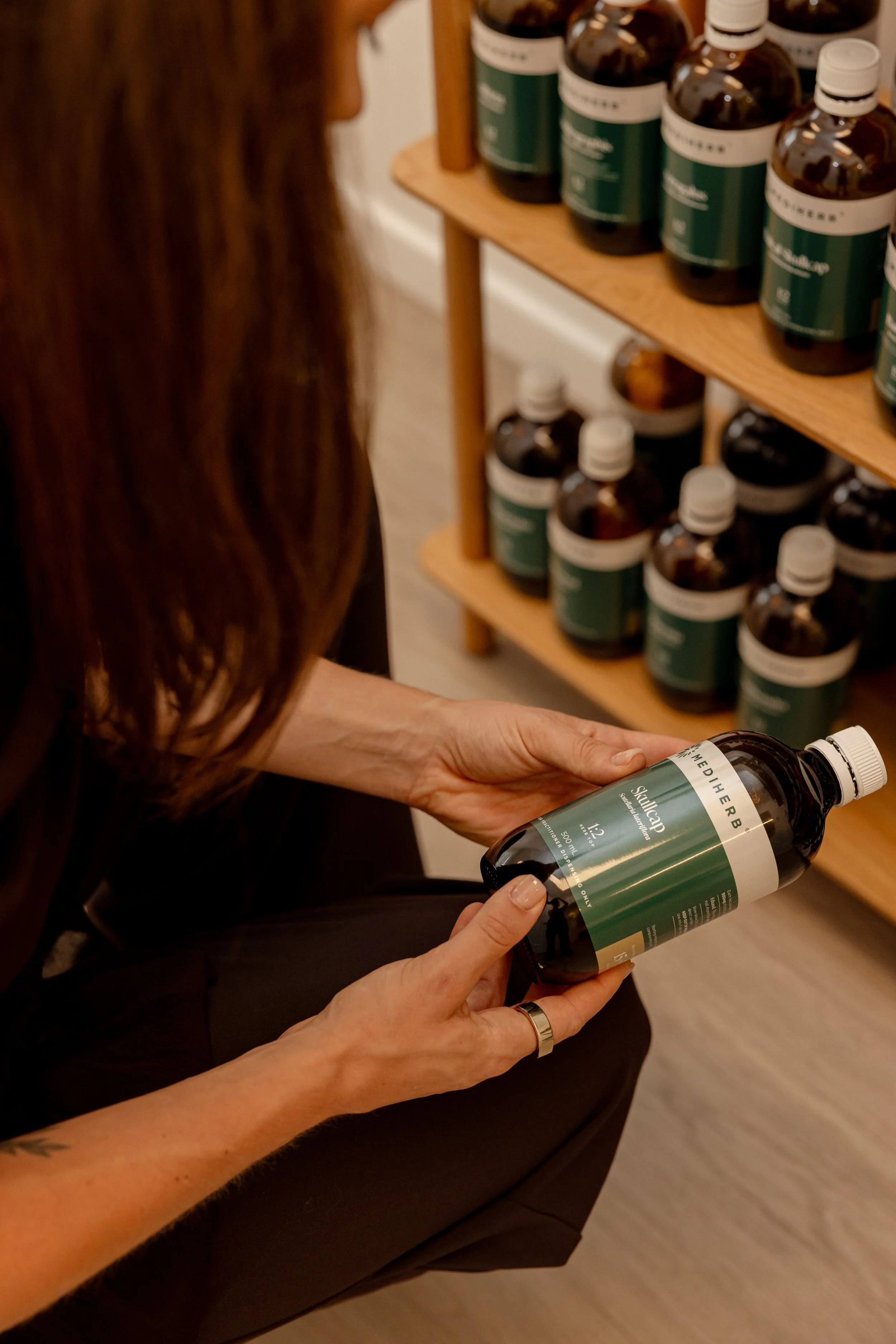 A cylindrical herbal product container with a minimalist label sitting on a wooden surface near a potted green and white variegated houseplant.