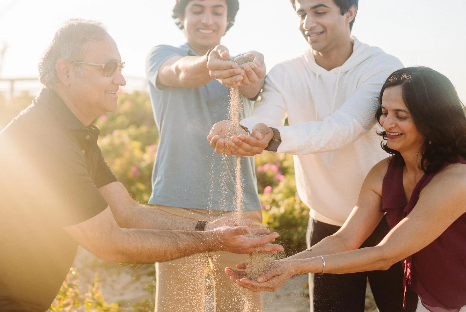 Parents and two grown sons pouring sand between their hands at sunset, Massachusetts family photography