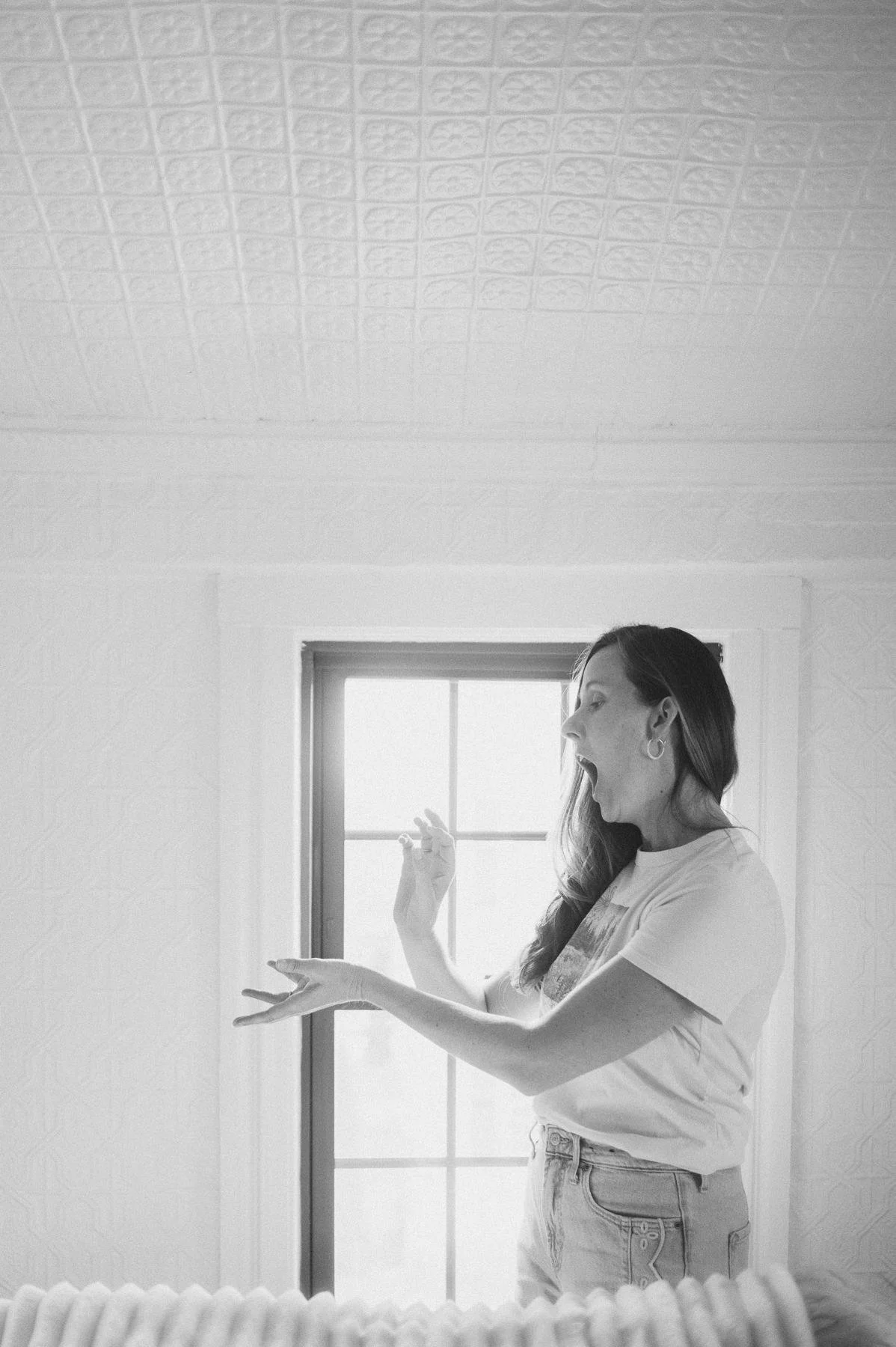 Black and white photo of a woman doing energy work with open hands and open mouth in front of a bright window, Massachusetts brand photography for women in business
