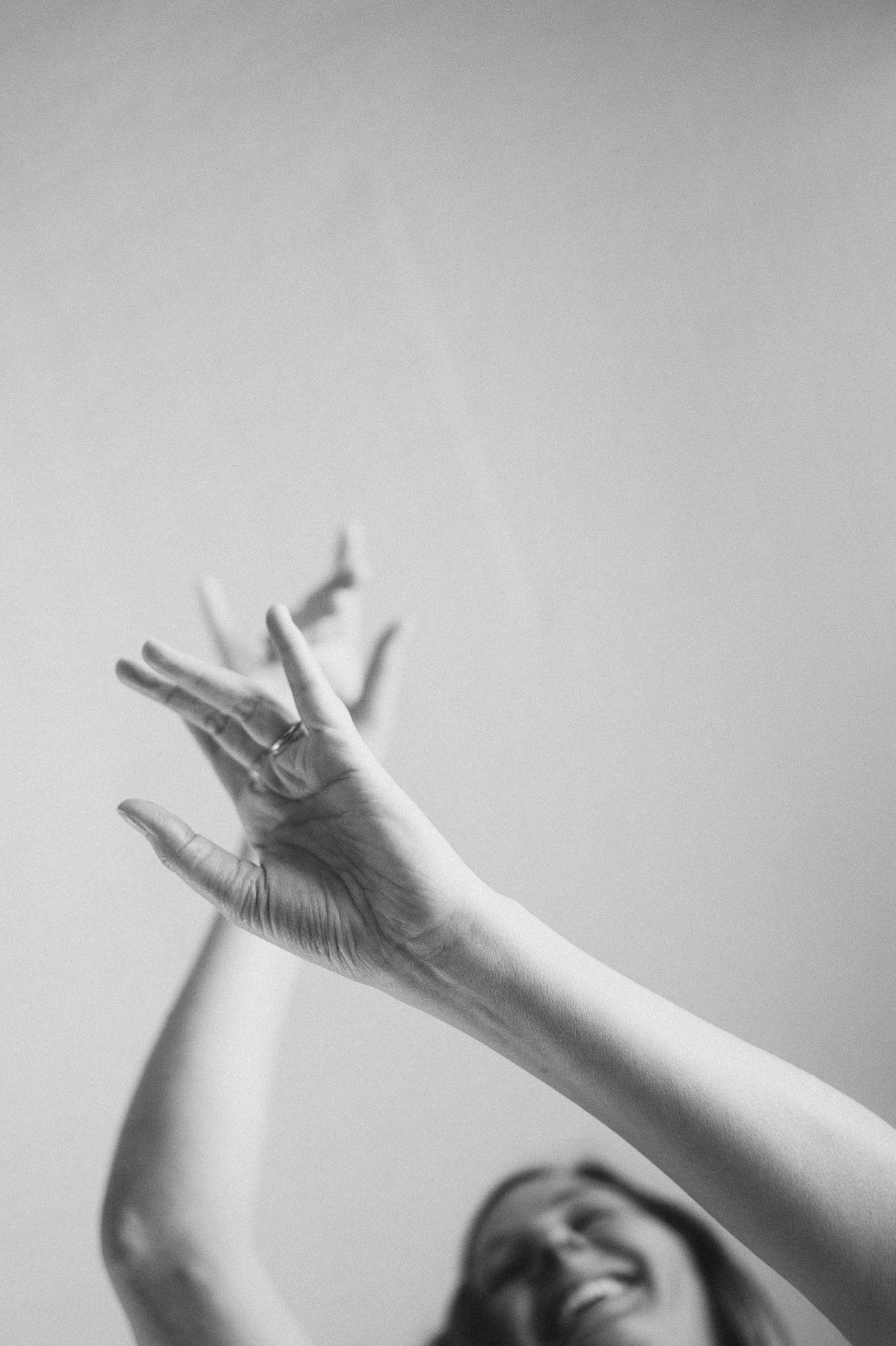 Black and white photo of a woman laughing with her hands raised overhead, captured in her flow, heart-centered branding photography