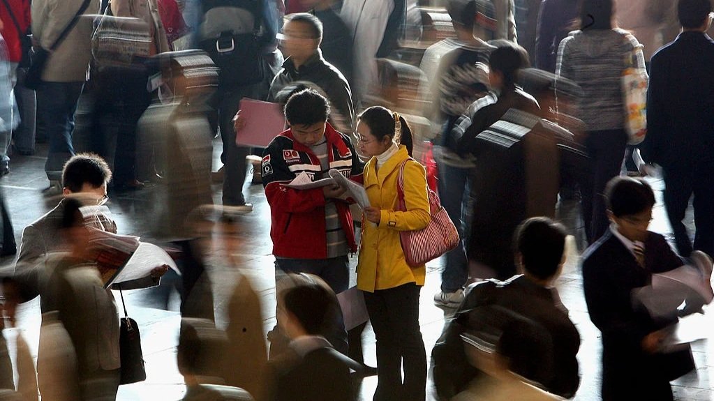 two college students browsing through a booklet while college students walk around them