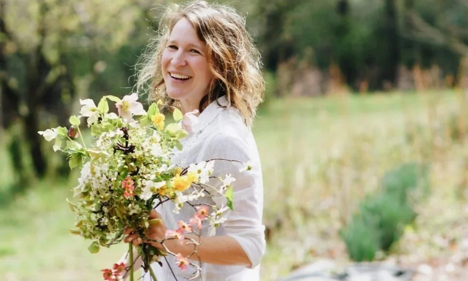 A woman smiling and holding a large bouquet of flowers outdoors in a garden or park.