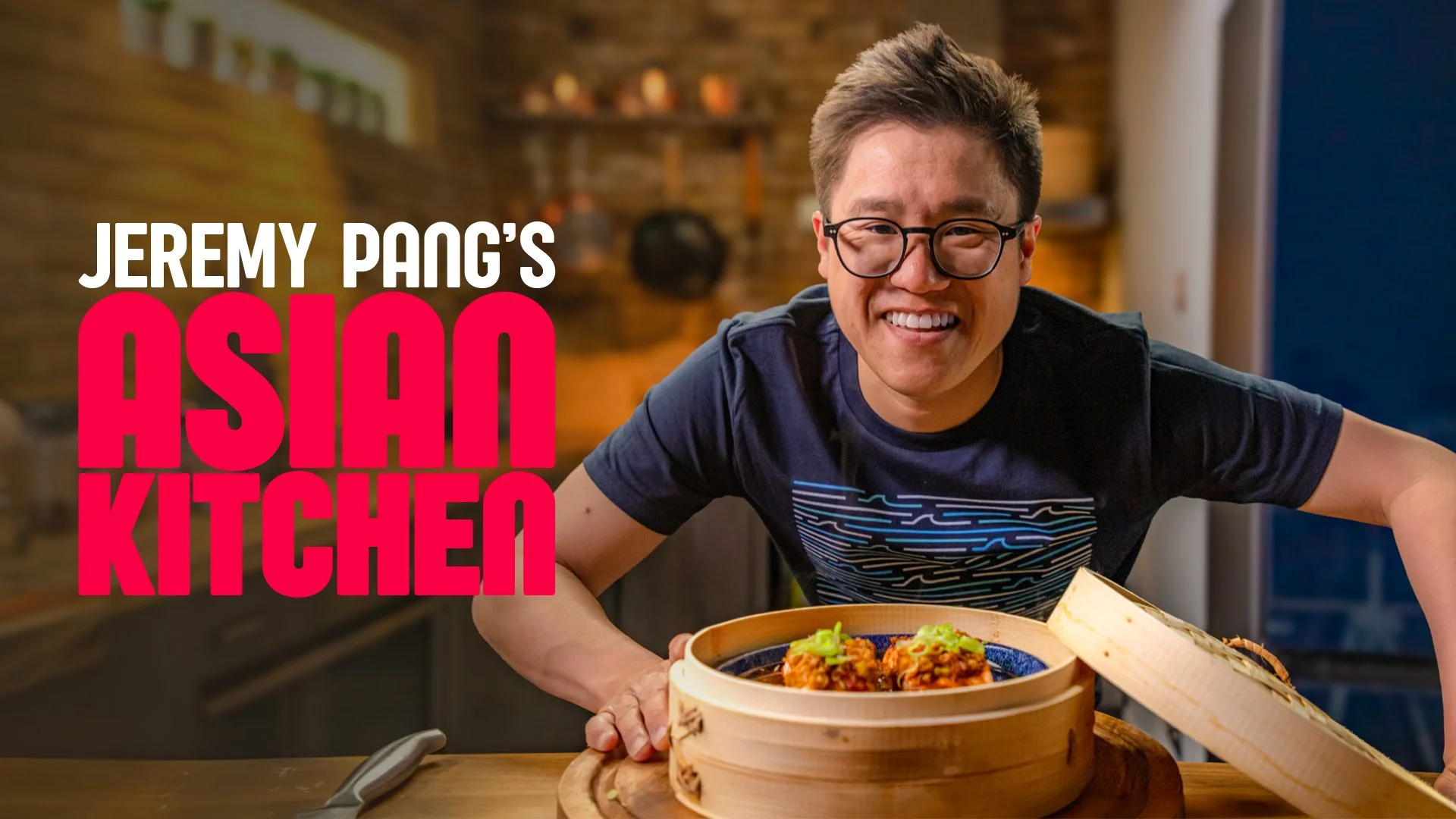Jeremy Pang smiling in a kitchen with a bamboo steamer containing Chinese dumplings in front of him.