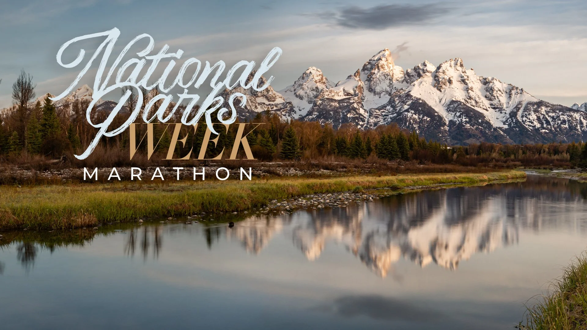 A scenic landscape of snow-capped mountains reflecting in a calm river with green grass and trees in the foreground. Overlaid text reads 'National Parks Week Marathon'.
